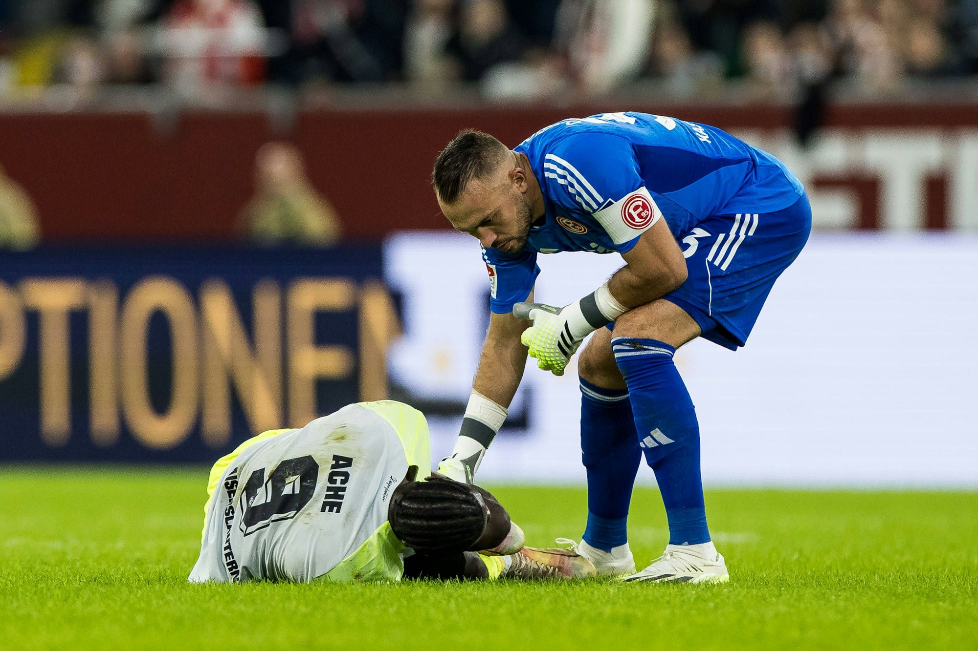Fortuna Düseldorfs Keeper Florian Kastenmeier beugt sich zum am Boden liegenden Kaiserslautern-Stürmer Ragnar Ache herab.