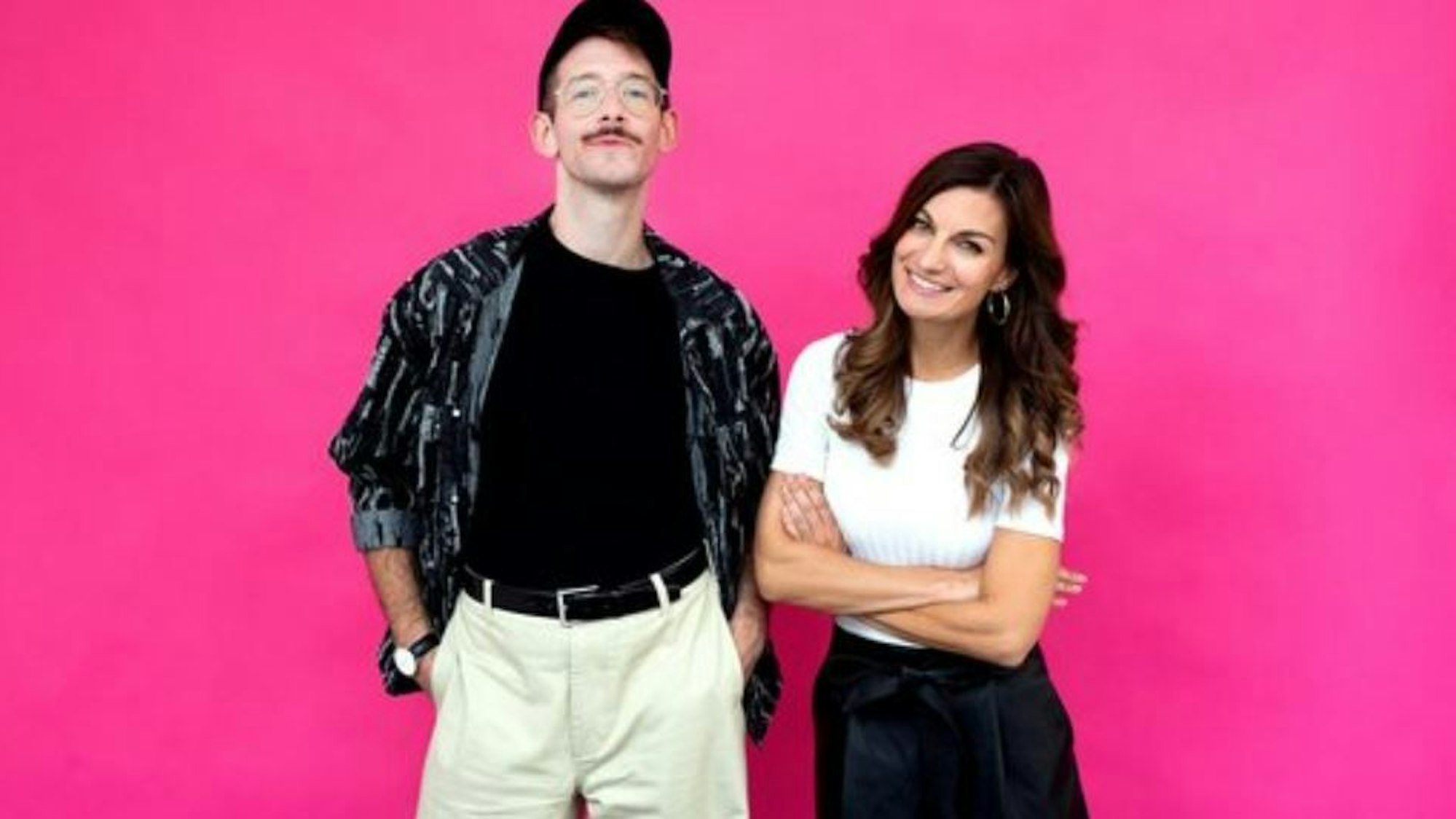 Benni Bauerdick (l.) und Freddie Schürheck stehen vor einer rosa Wand und lachen in die Kamera.