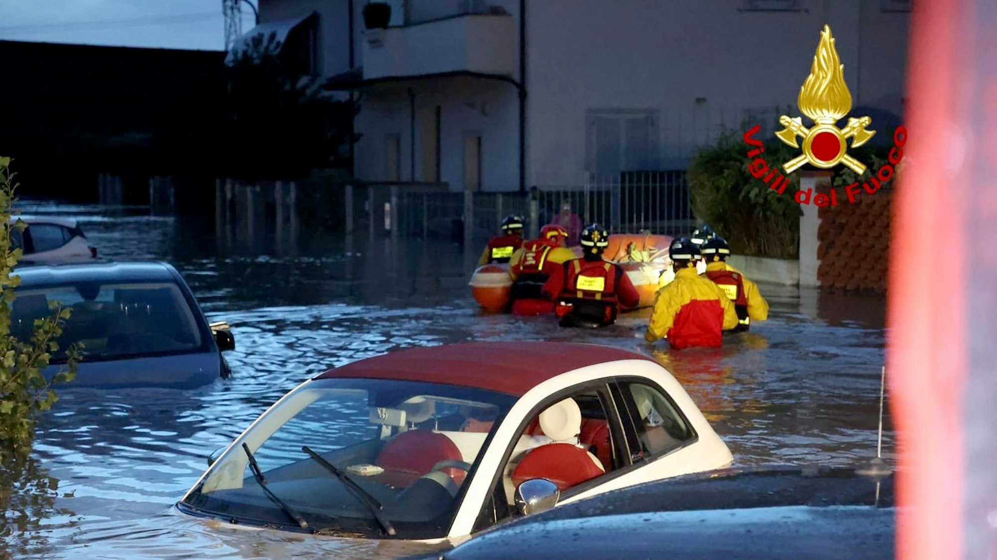 Feuerwehrleute schieben ein Schlauchboot durch eine überschwemmte Straße, in der zahlreiche Autos unter Wasser stehen. Schwere Unwetter mit heftigen Regenfällen haben die mittelitalienische Region Toskana in der Nacht zum Freitag heimgesucht.