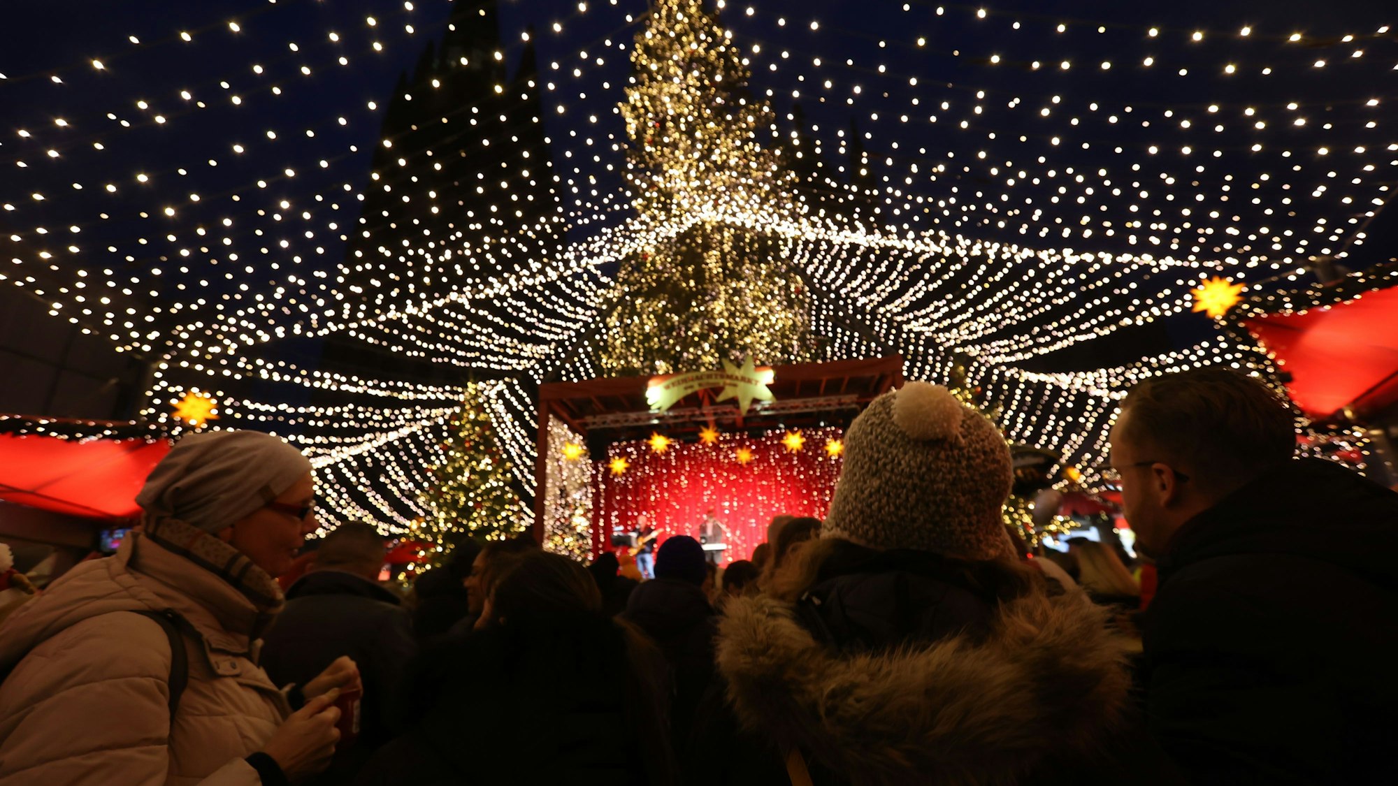 Menschen stehen vor der Bühne. Im Hintergrund ein erleuchteter Weihnachtsbaum.