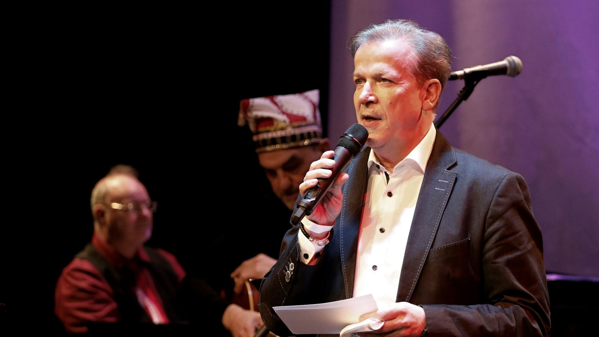 Ein Mann im dunklen Anzug steht mit Zetteln und Mikrofon auf einer Bühne und hält eine Rede.