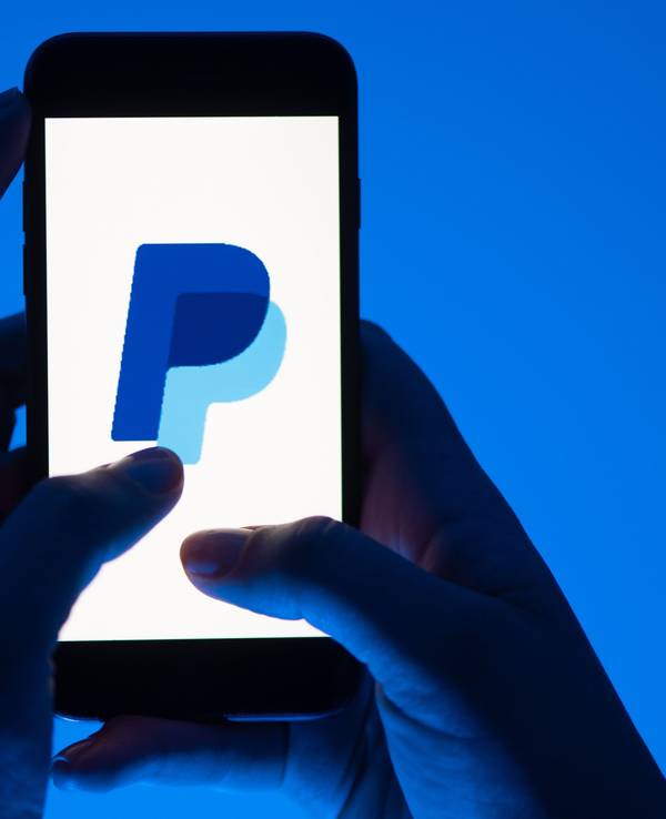 Eine Frau hält ein Smartphone mit dem Logo des Bezahldienstes Paypal.