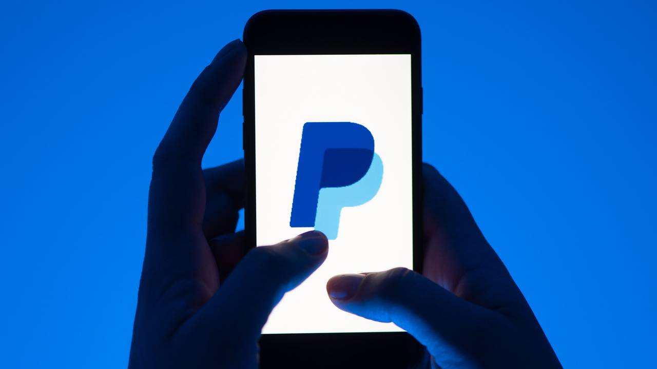 Eine Frau hält ein Smartphone mit dem Logo des Bezahldienstes Paypal.