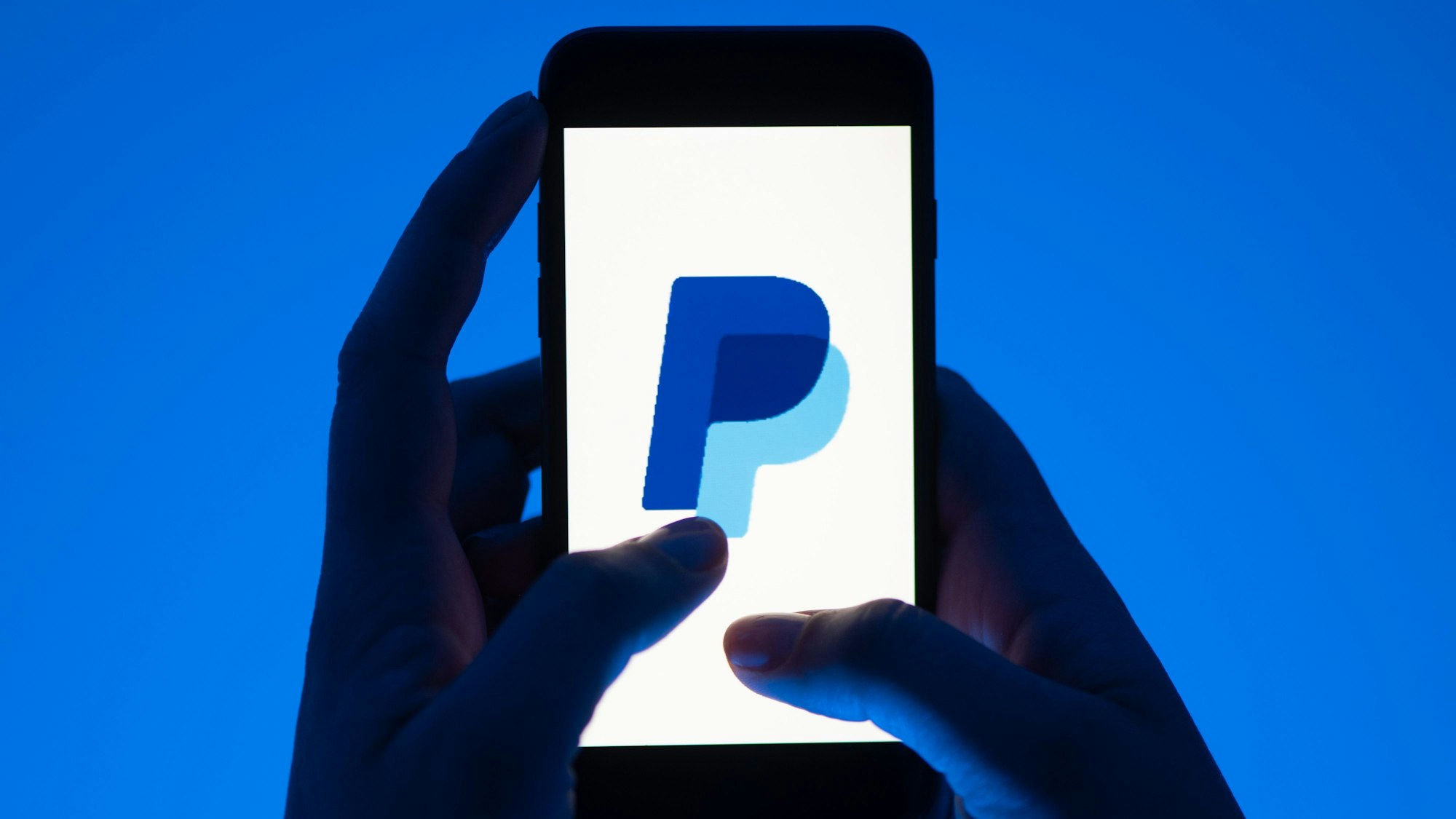 Eine Frau hält ein Smartphone mit dem Logo des Bezahldienstes Paypal.