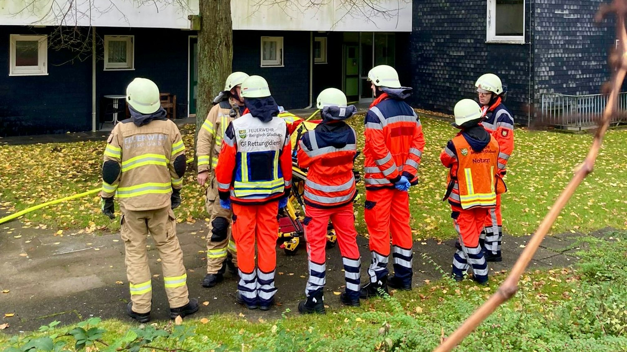 Sieben Einsatzkräfte der Feuerwehr stehen mit Schlauch vor einem Wohnhaus und löschen.
