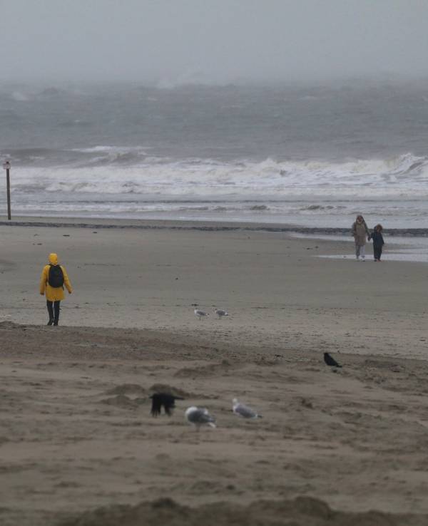 Eine Spaziergängerin geht bei stürmischem Wetter am Strand spazieren.