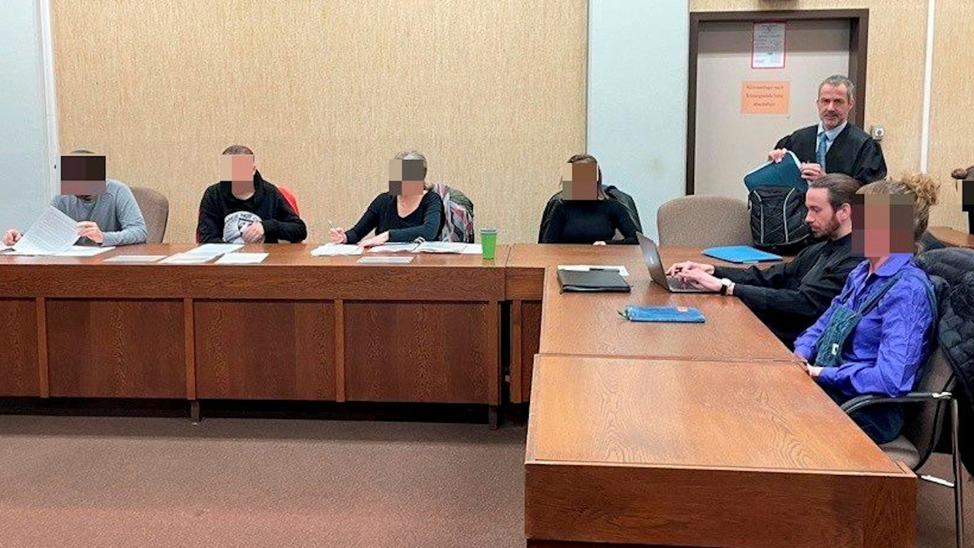 Fünf Personen sitzen im Gericht auf der Anklagebank neben zwei Anwälten.