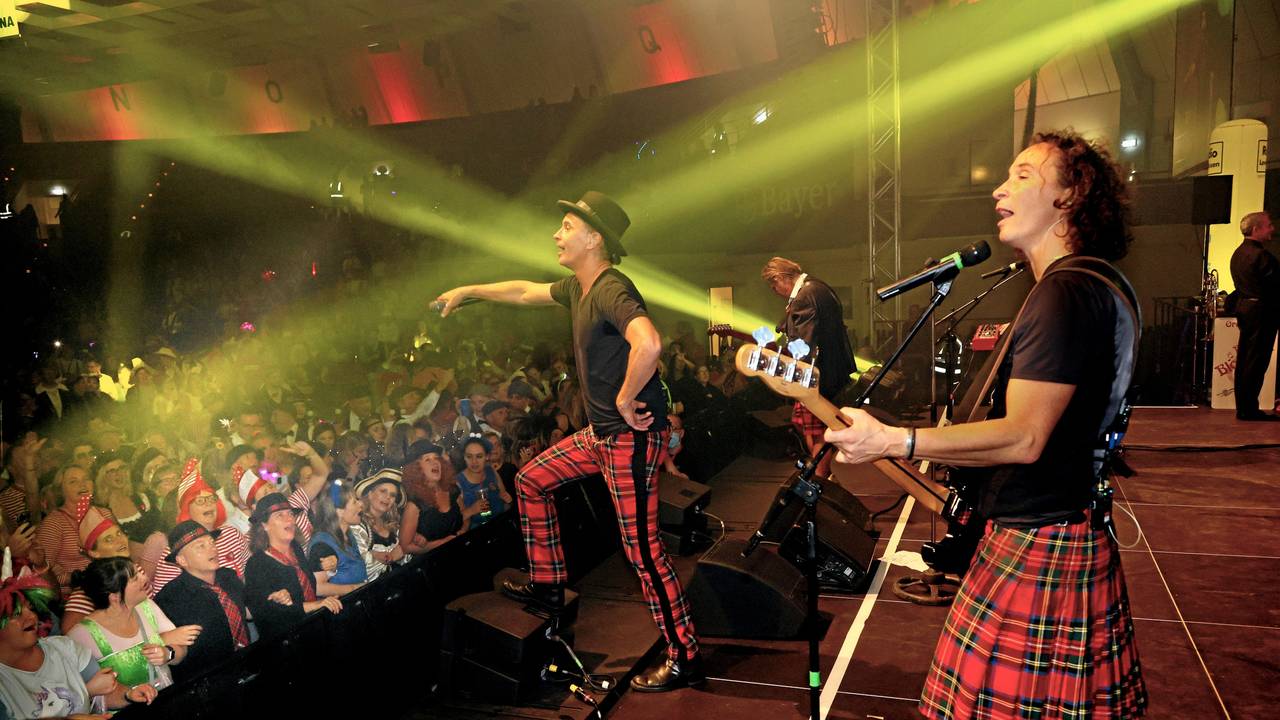 Die Band Brings steht bei einem Konzert in einer Halle auf der Bühne und singt mit dem Publikum.