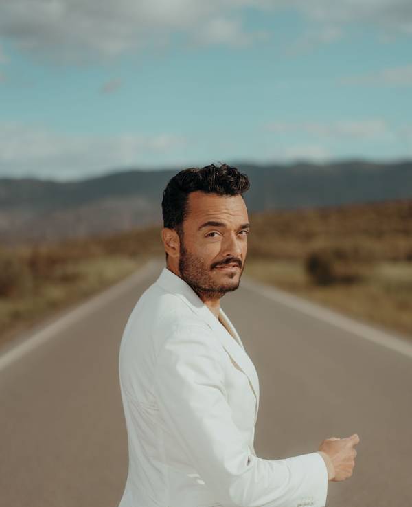 Giovanni Zarrella trägt einen weißen Anzug und blickt auf einer Straße über die Schulter in die Kamera.