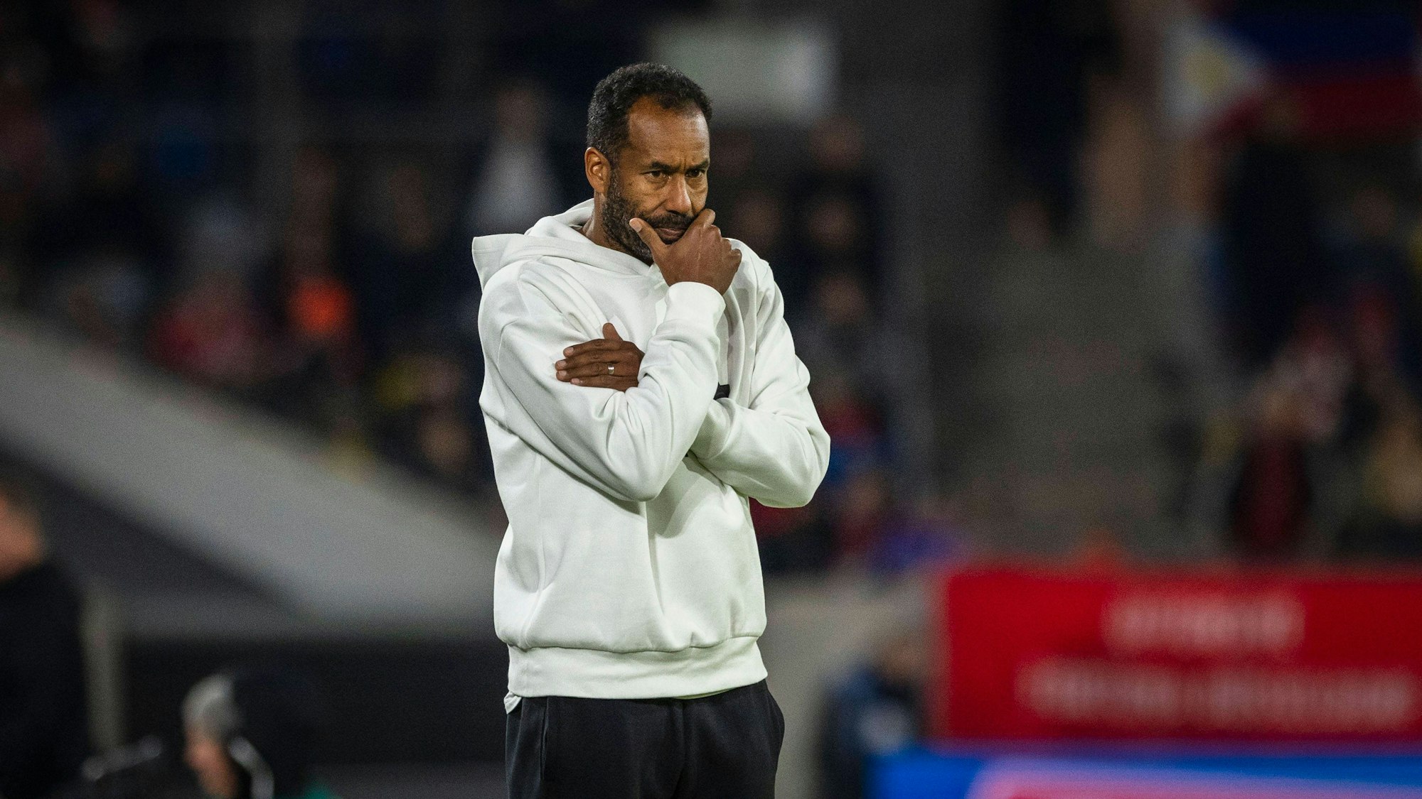 Daniel Thioune hält sich beim Spiel von Fortuna Düsseldorf nachdenklich die Hand vors Gesicht.
