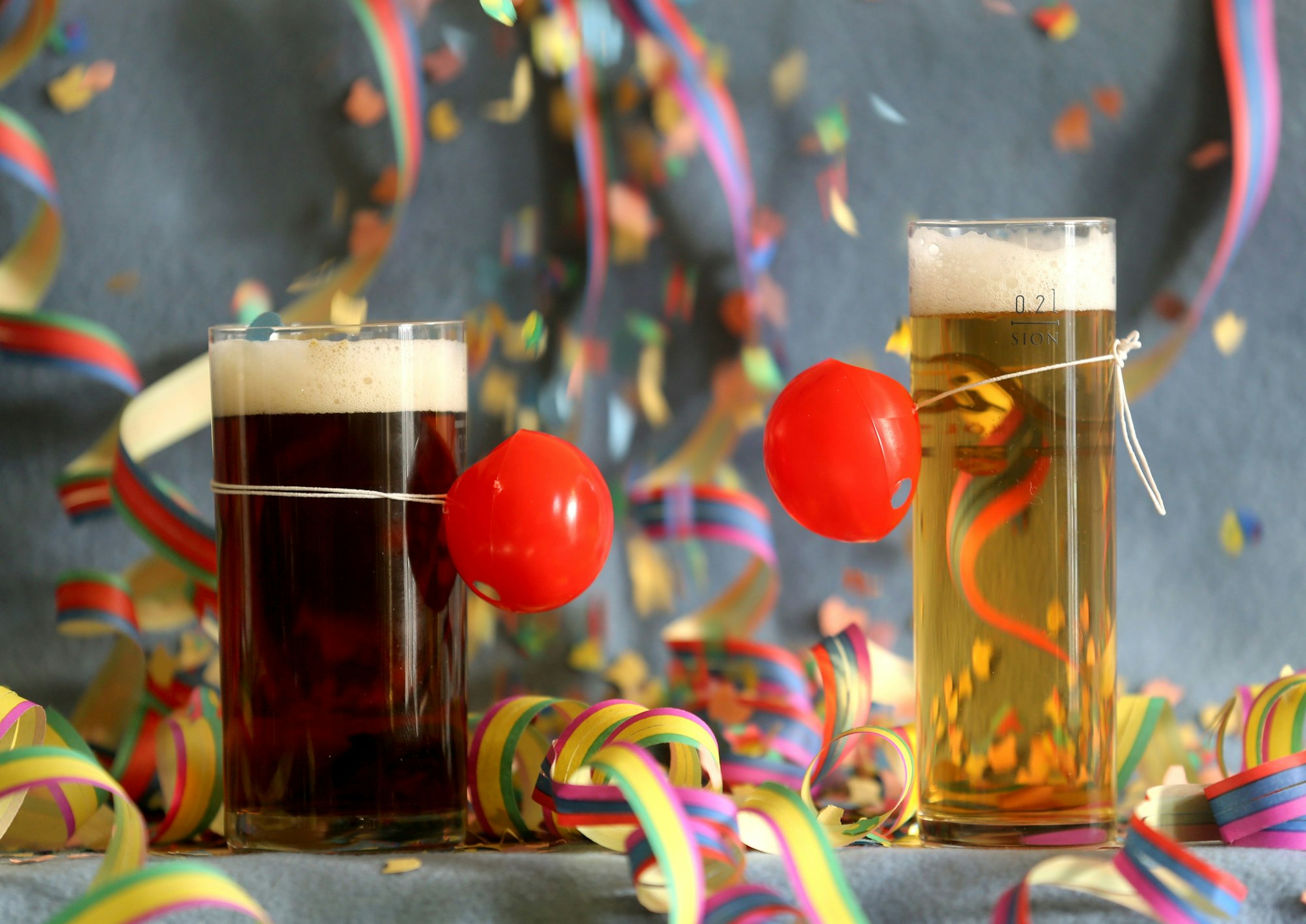 Hier zu sehen: Ein Altbier und ein Kölsch stehen, mit roten Pappnasen geschmückt, auf einem bunt dekorierten Tisch.