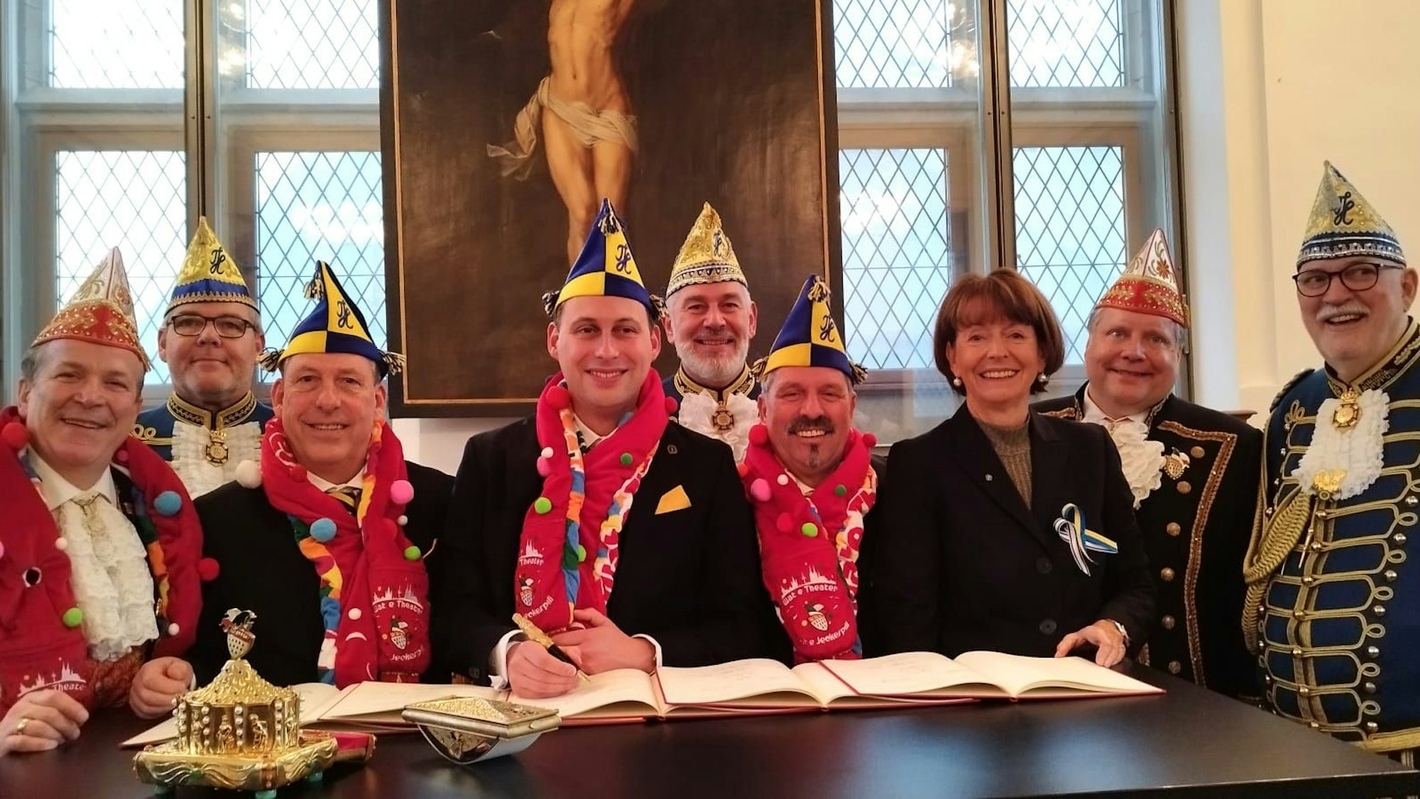 Neun Personen an einem Schreibtisch, dabei wird ein Dokument unterschrieben.