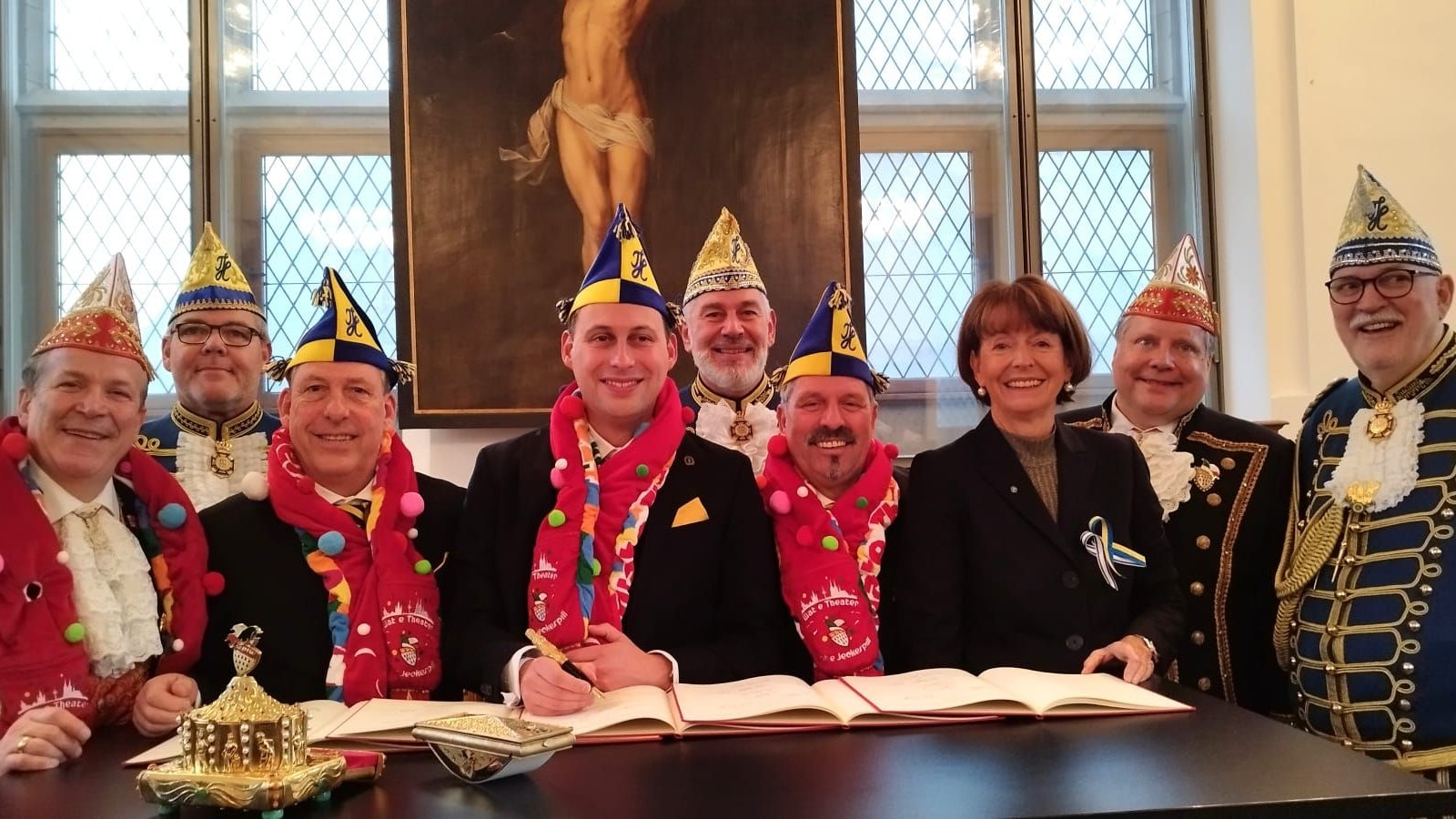 Neun Personen an einem Schreibtisch, dabei wird ein Dokument unterschrieben.