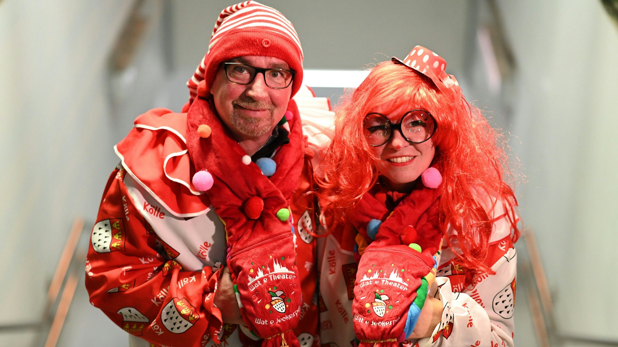Zwei verkleidete Menschen ganz in rot halten sich im Arm und lachen in die Kamera.