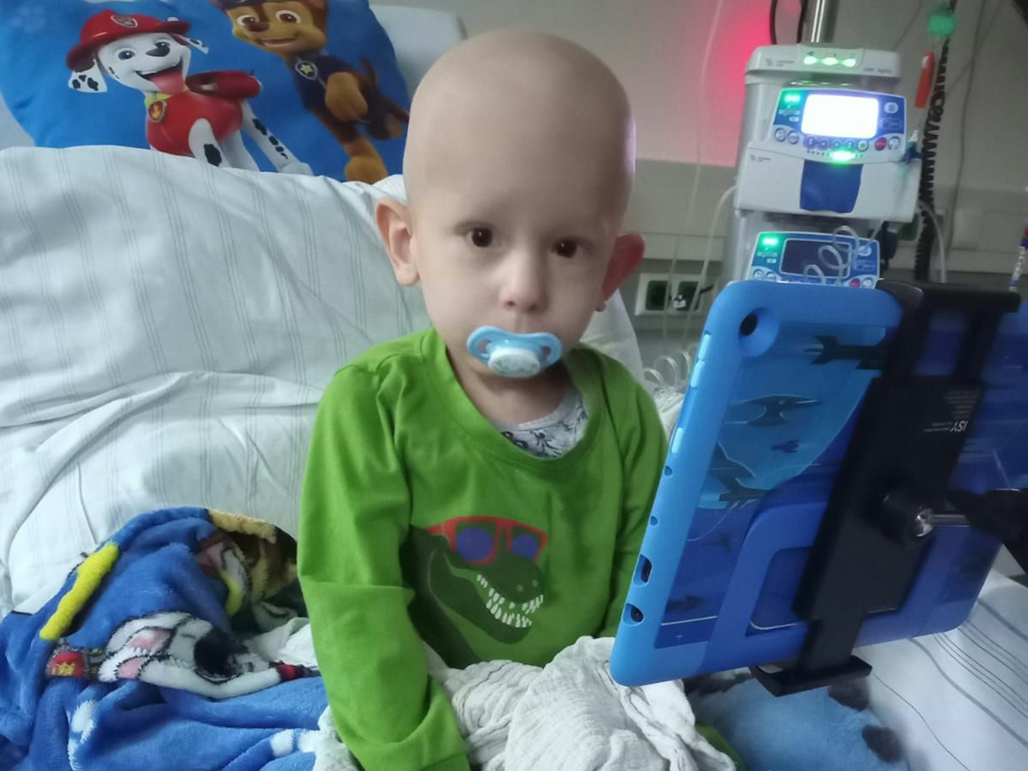 Dean-Connor sitzt auf einem Bett im Krankenhaus. Er schaut mit Schnuller in die Kamera.