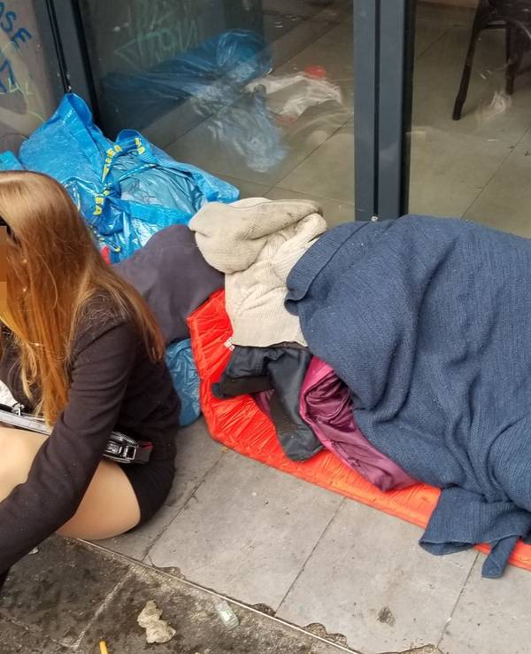 Ein Mädchen sitzt am 11.11.2023 in einem Eingang zu einer Gastro auf der Zülpicher Straße – hinter ihr liegt ein schlafender Obdachloser.