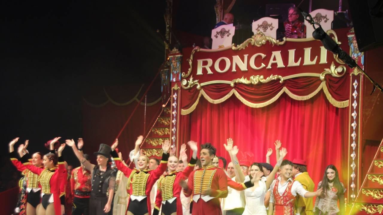 Artistinnen und Artisten stehen in der Manege des Circus Roncalli und winken.