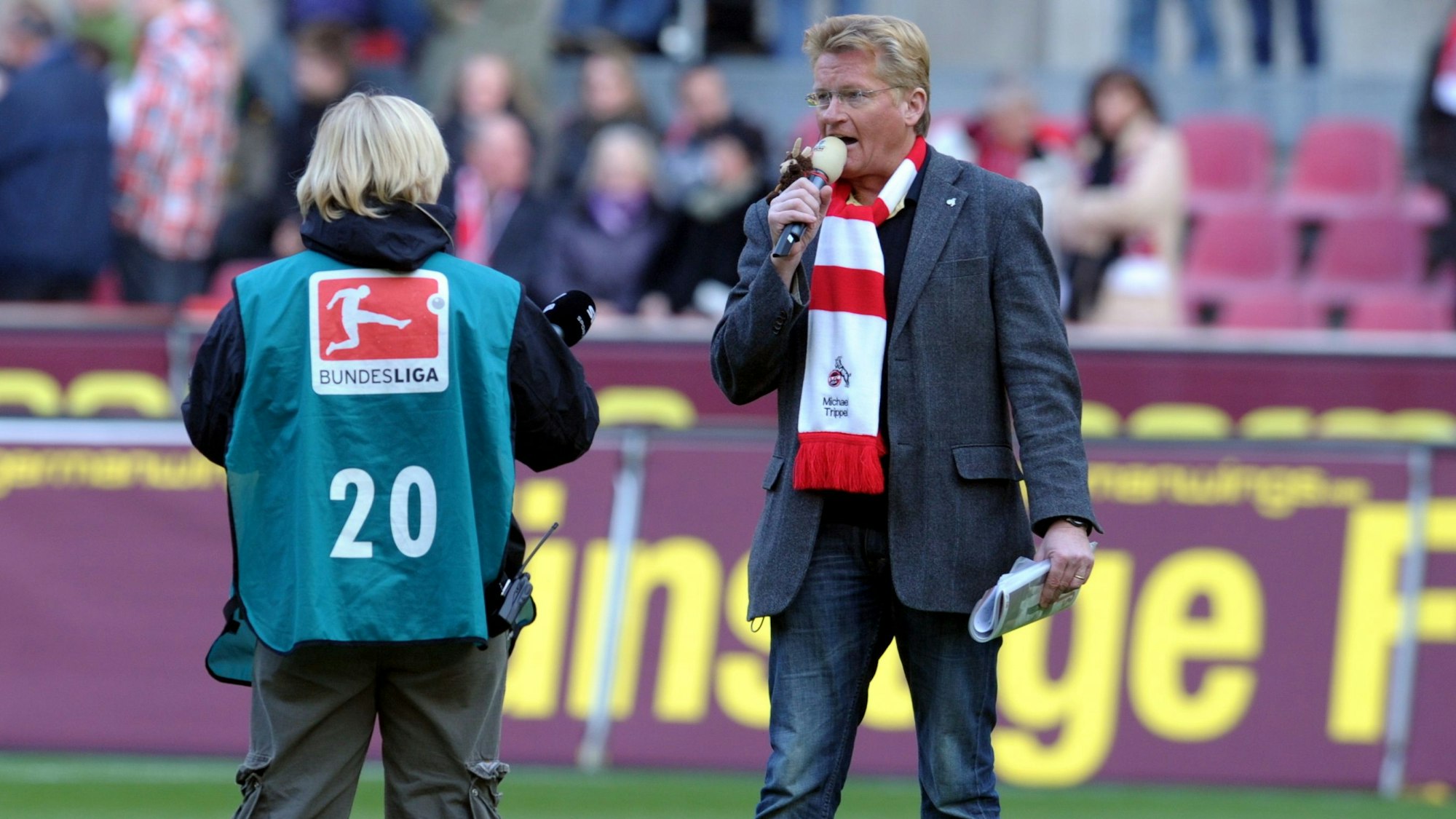 Stadionsprecher des 1. FC Kölns Michael Trippel steht mit Mikrofon in einem Fußball-Stadion.