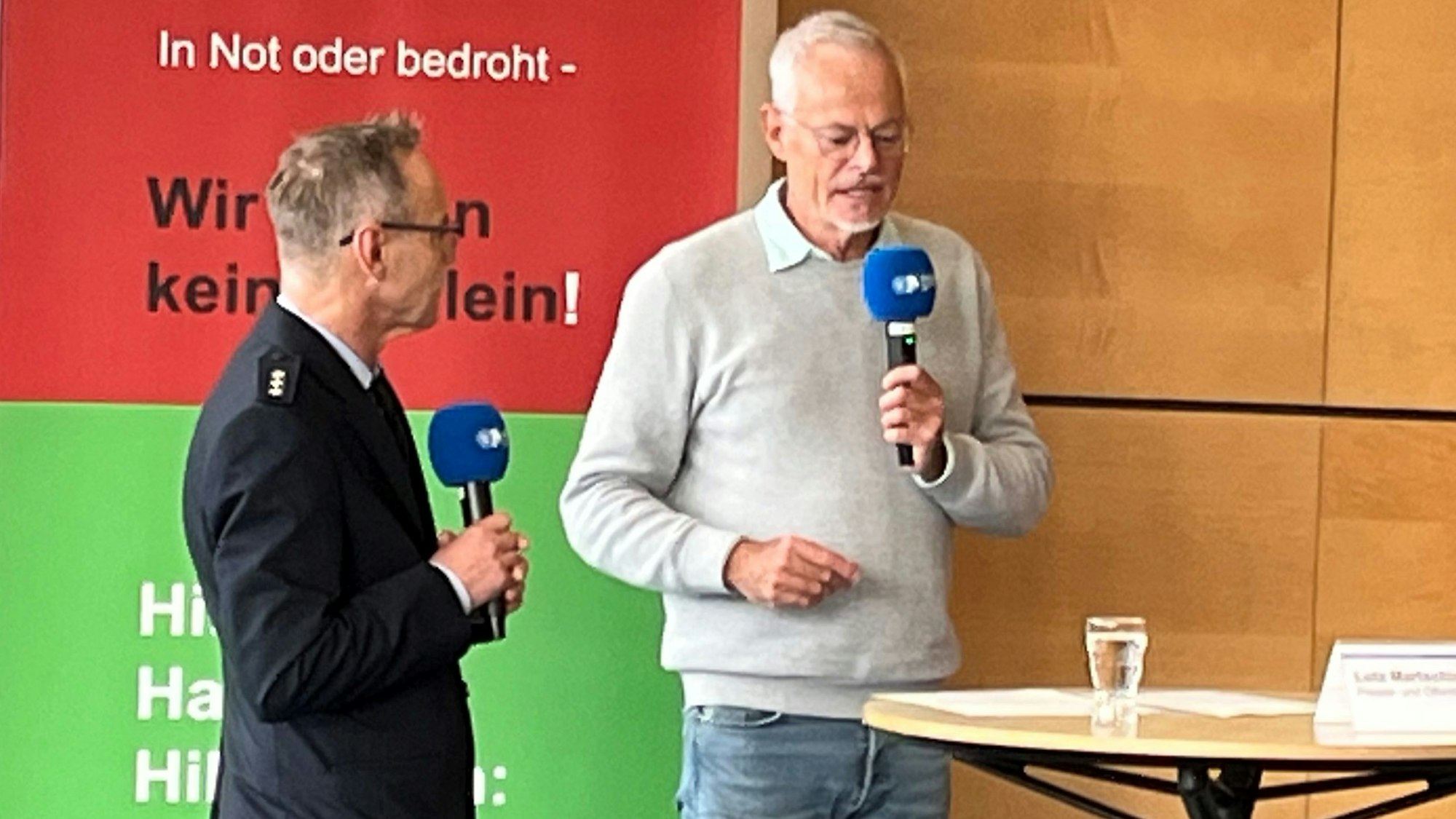 Ein Mann spricht in ein Mikrofon, neben ihm steht ein weiterer Mann.
