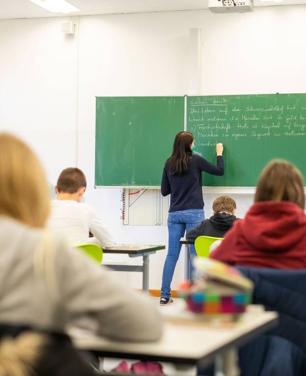 Eine Lehrerin schreibt etwas an die Tafel, die Schulkinder schreiben mit.