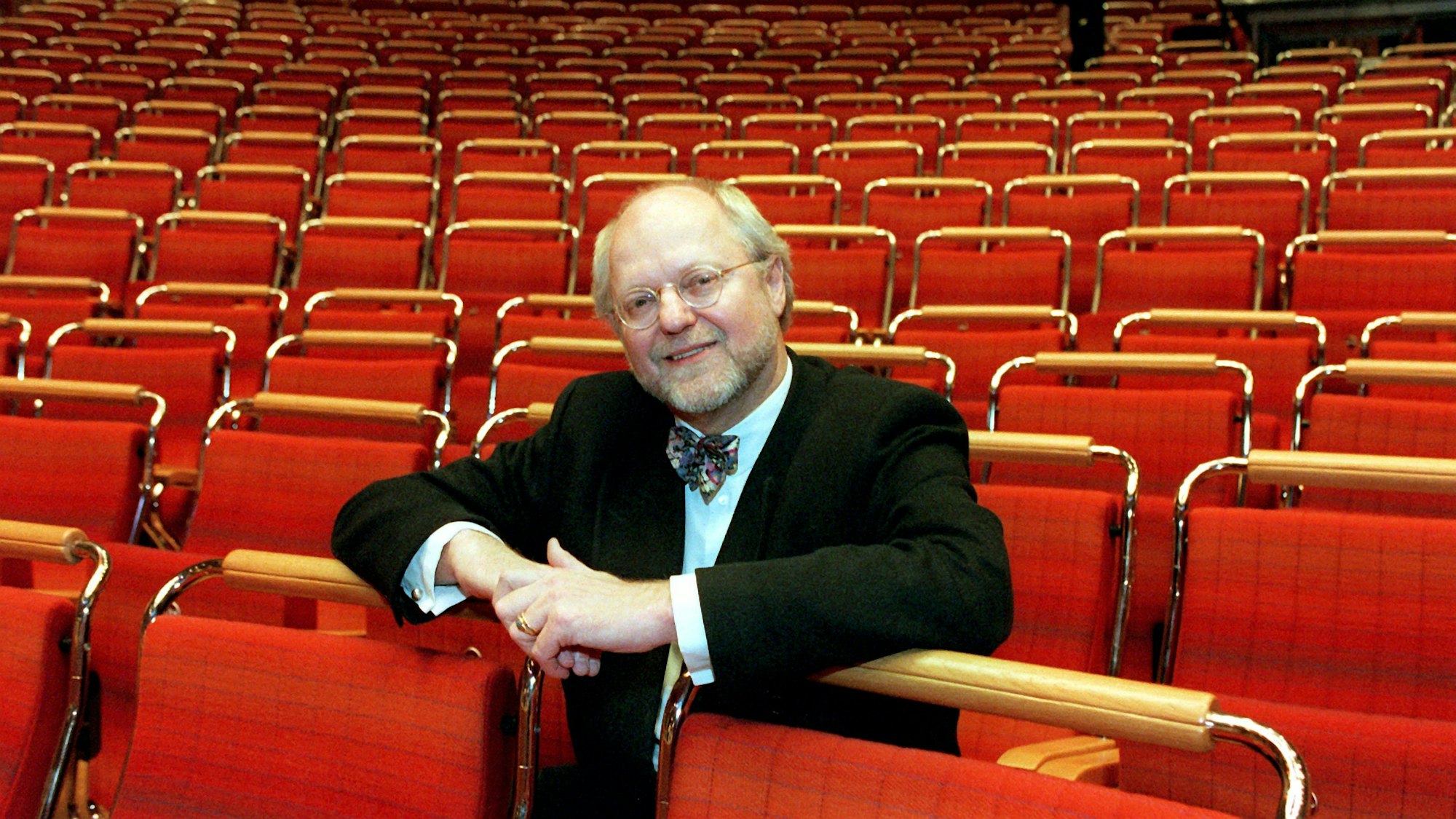 Franz Xaver Ohnesorg sitzt auf einem roten Stuhl im leeren Kölner Konzerthaus und schaut in die Kamera.