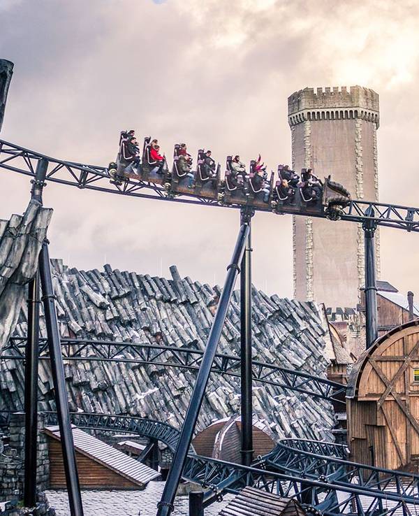 Blick von unten auf die Achterbahn Taron im Phantasialand. Im Hintergrund ist das Mystery Castle zu sehen.