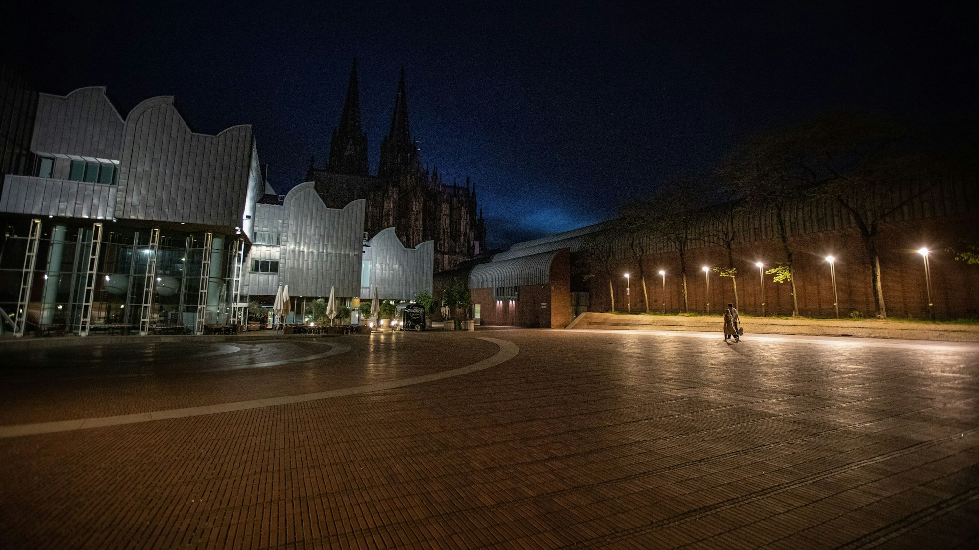 Zwei Personen gehen über den ansonsten menschenleeren Heinrich-Böll-Platz am Sonntagabend.
