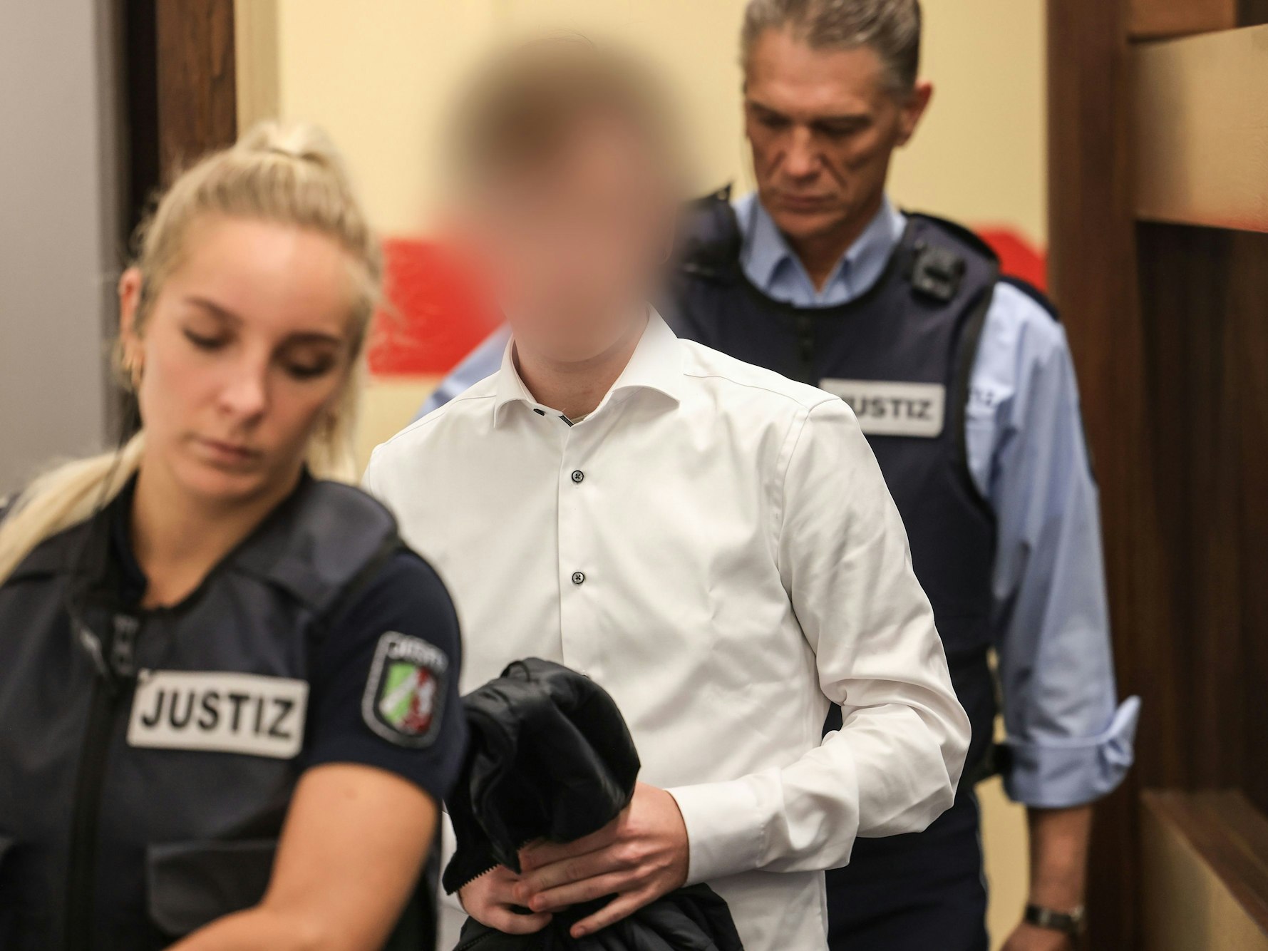 Der Angeklagte wird von zwei Justizangestellten in den Gerichtssaal geführt.