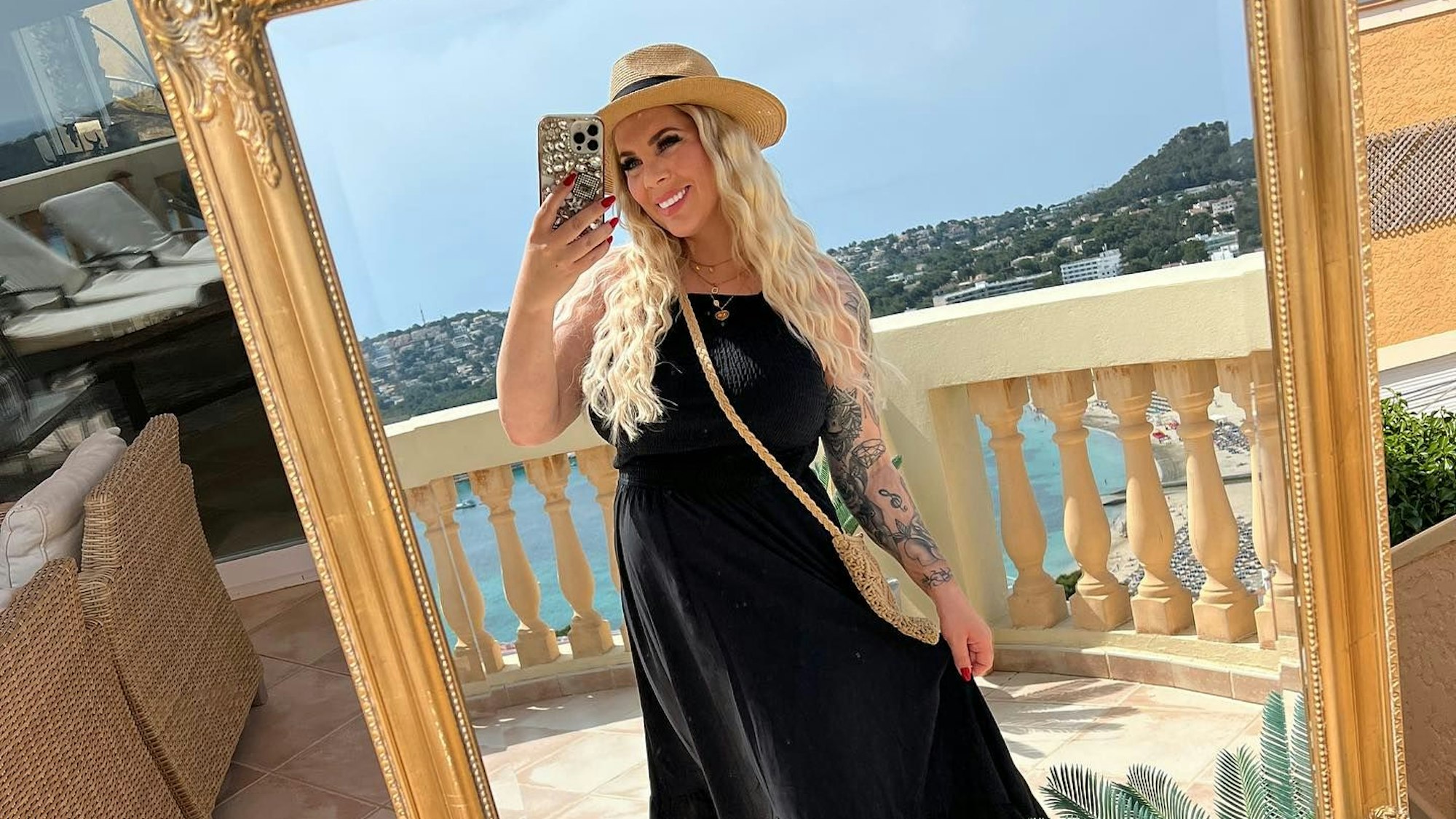 Jenny Frankhauser posiert in einem langen schwarzen Sommerkleid und Hut vor einem Spiegel.