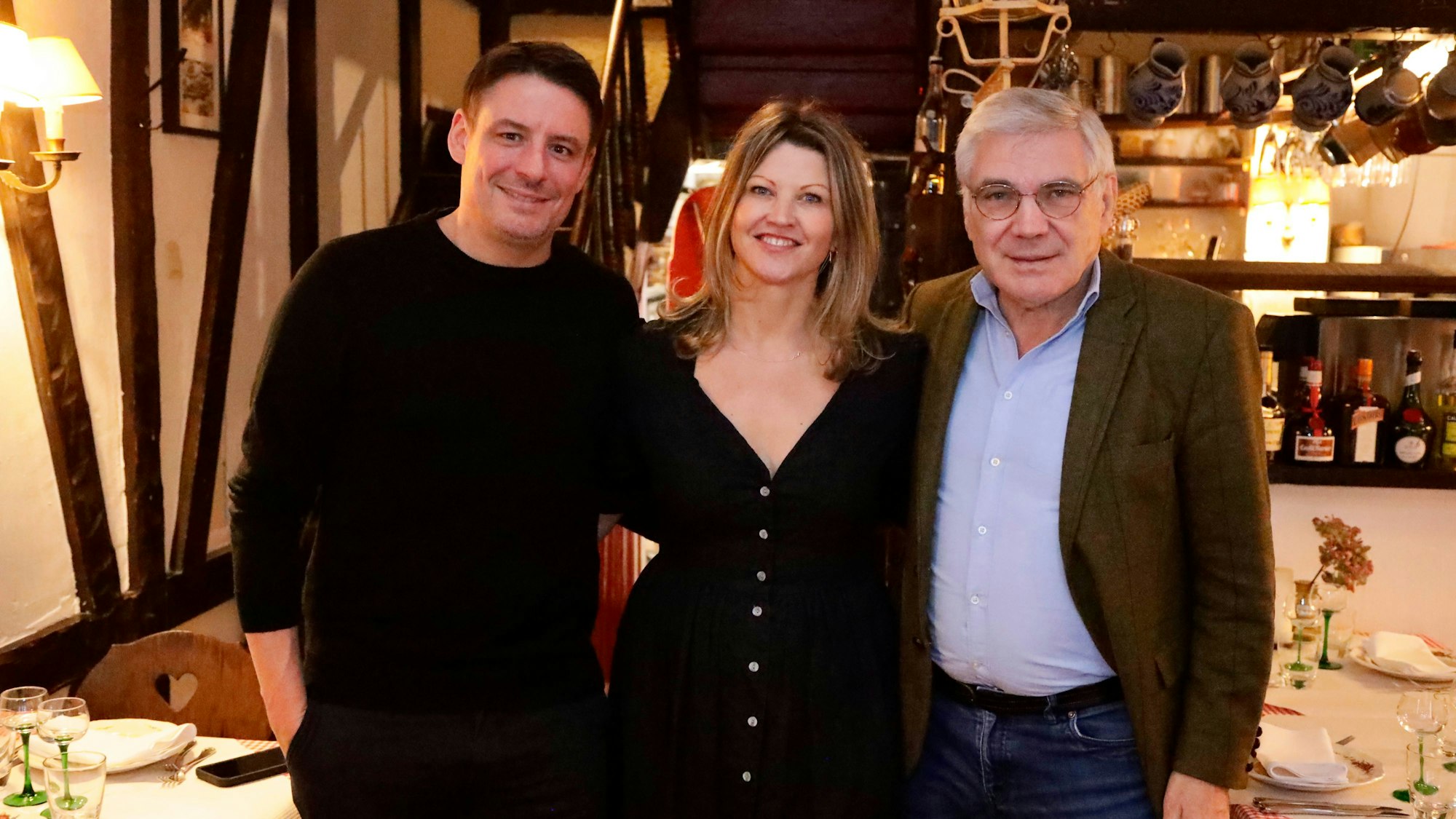 Zwei Männer und eine Frau stehen in einem Restaurant und halten sich im Arm.