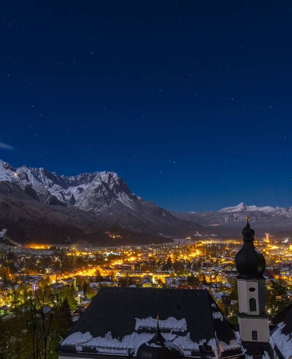 Blick auf das bayerische Garmisch-Partenkirchen bei Nacht. Die Stadt ist umrahmt von den schneebedeckten Alpen.