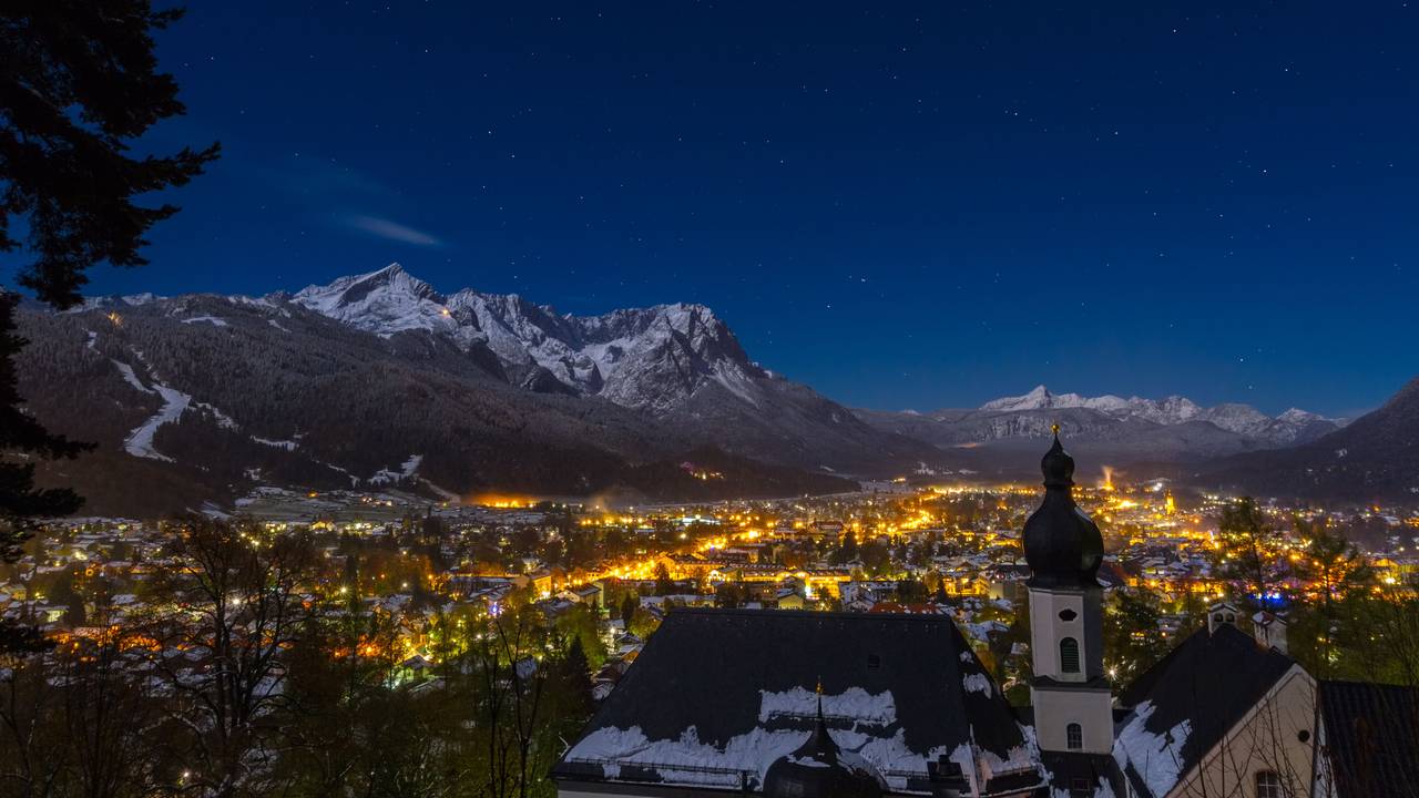 Blick auf das bayerische Garmisch-Partenkirchen bei Nacht. Die Stadt ist umrahmt von den schneebedeckten Alpen.