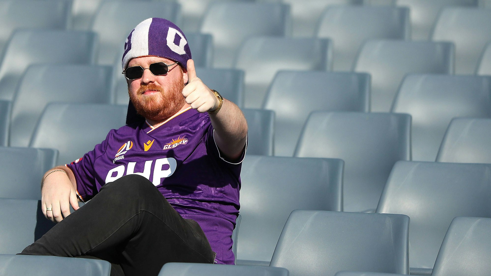 Perth Glory Fan sitzt alleine auf der sonnigen Tribüne und zeigt einen Daumen hoch.