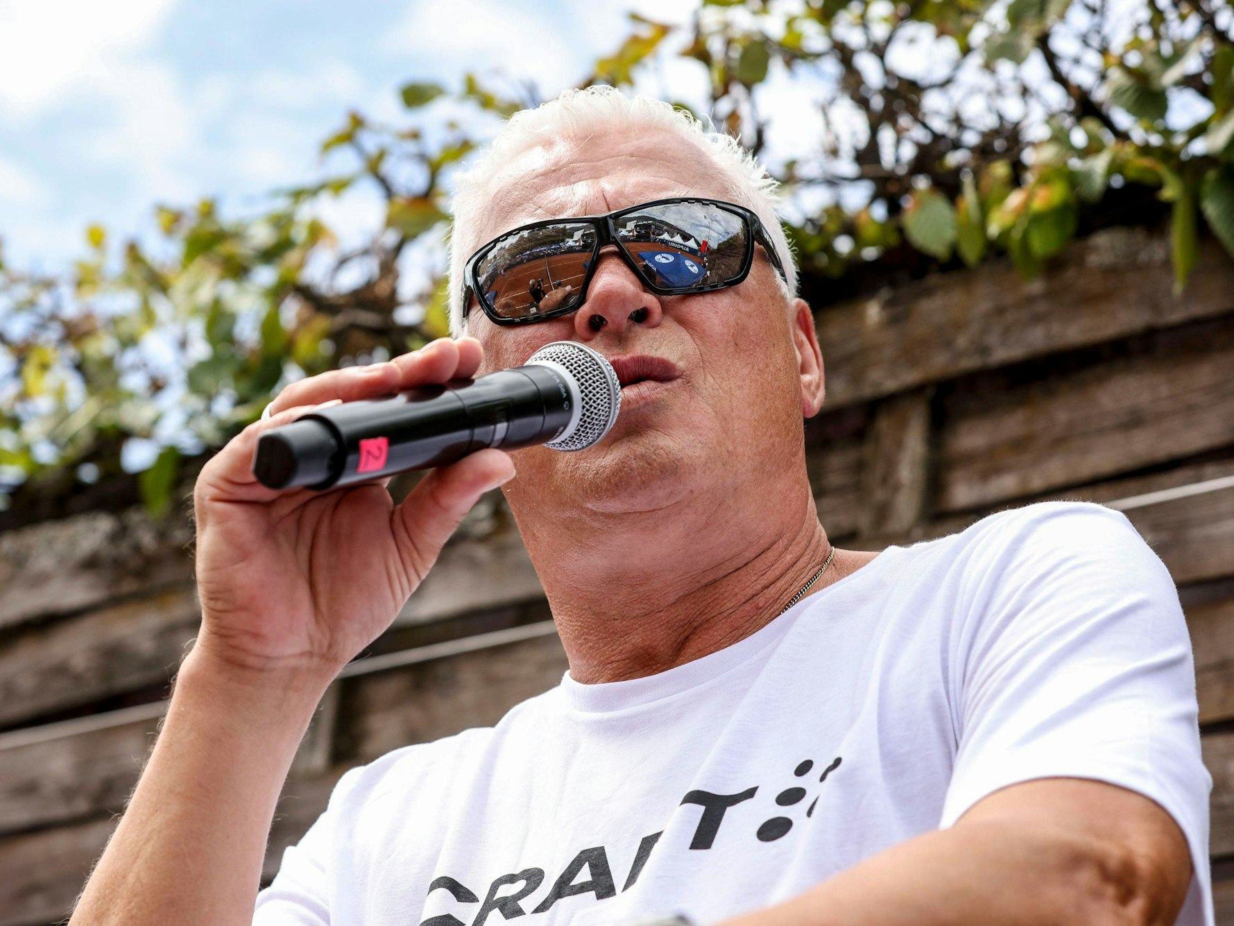 Toni Polster mit Sonnenbrille im Gesicht und Mikrofon in der Hand.