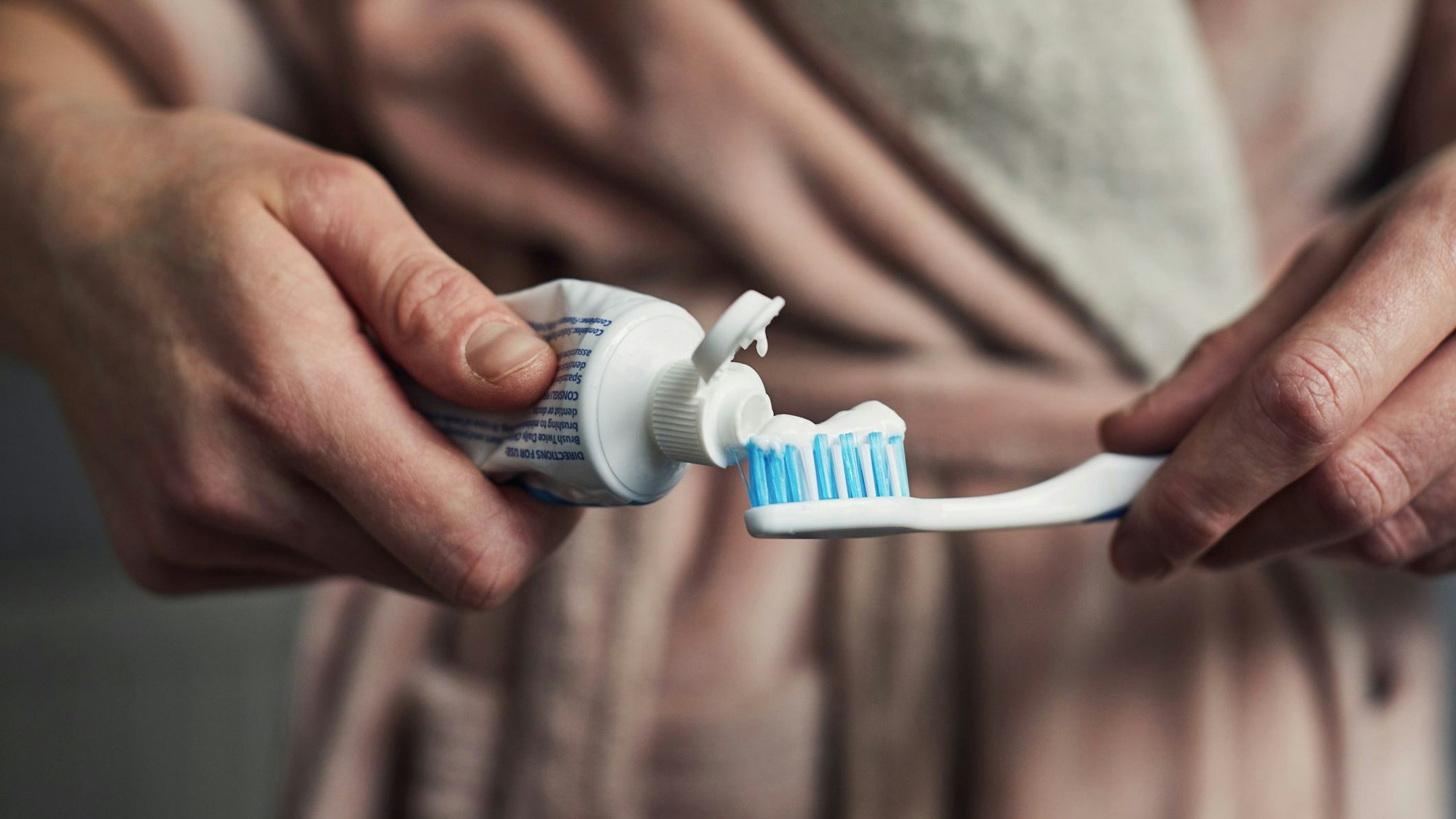 Auf dem Foto drückt ein Mann Zahnpasta aus der Tube auf seine Zahnbürste.