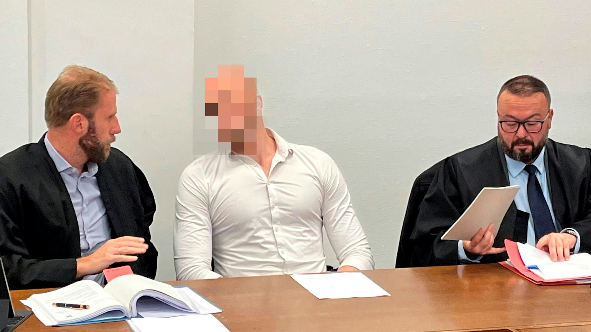 Der Angeklagte sitzt zwischen seinen beiden Anwälten.