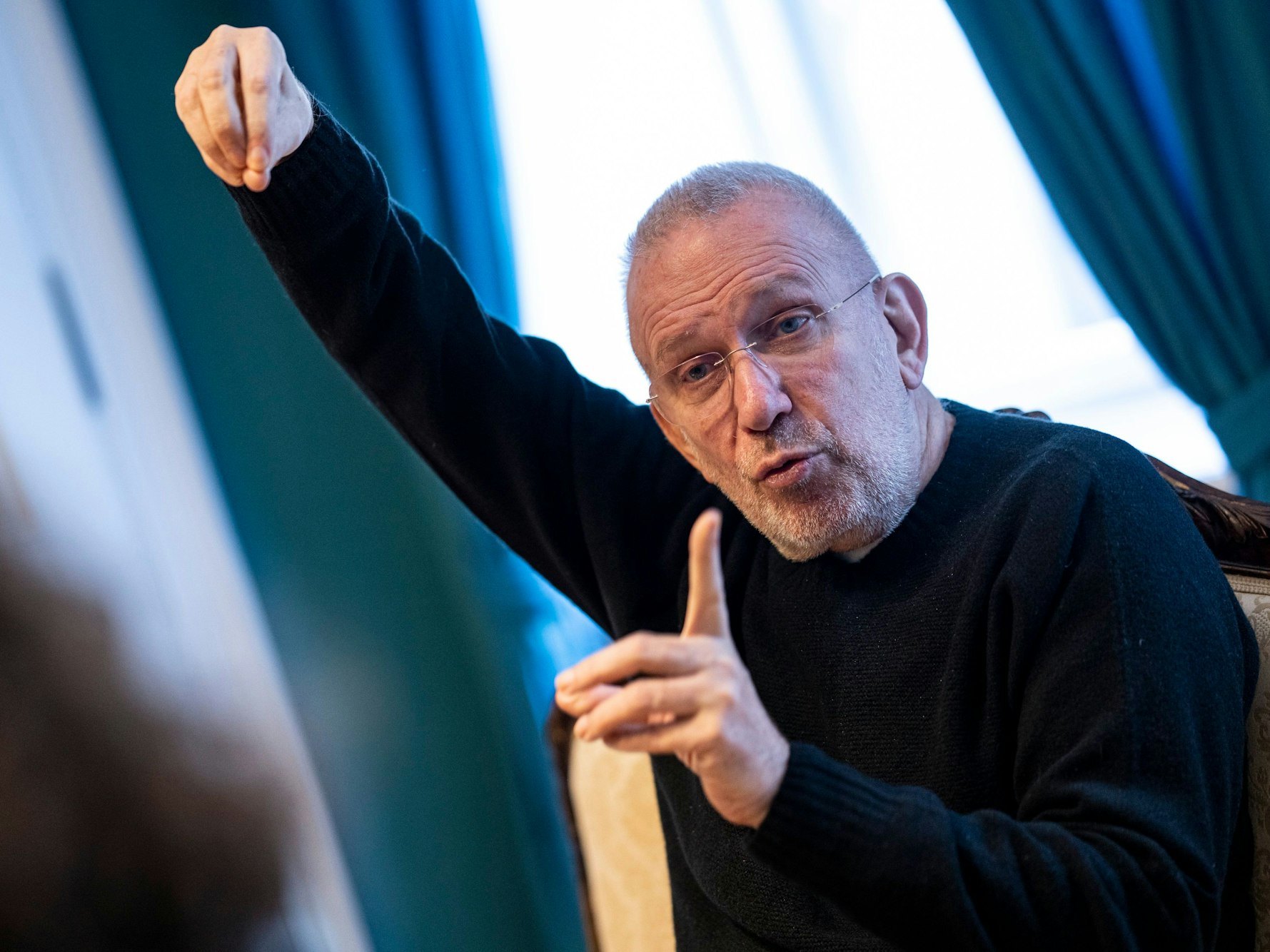 Der französische Modedesigner Jean Paul Gaultier sitzt im schlichten Outfit bei einem Interview und gestikuliert mit seinen Fingern.