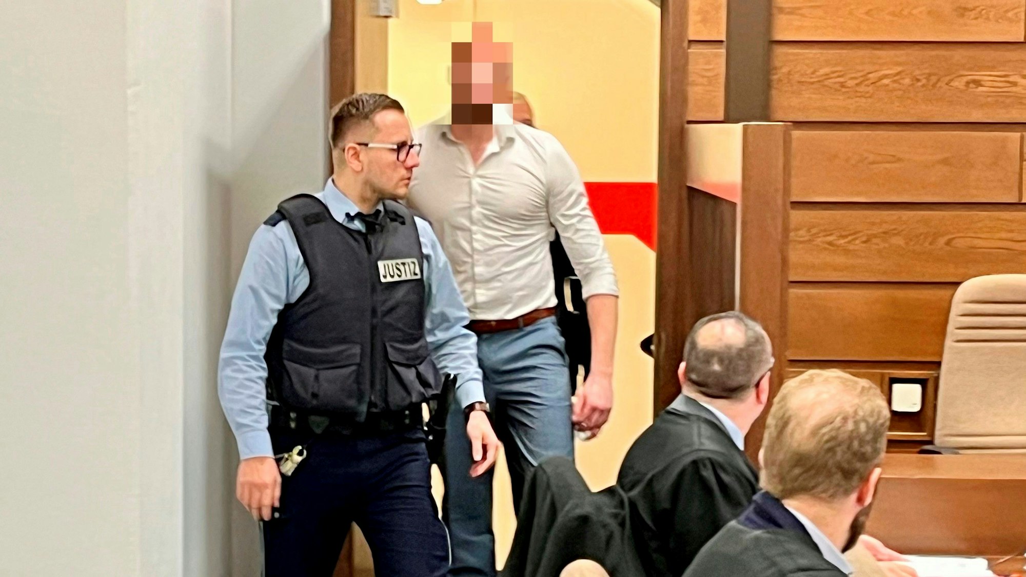 Zwei Wachtmeister bringen einen Mann in den Gerichtssaal.