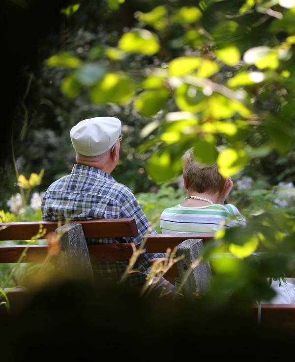 Ein älteres Paar sitzt im Kurpark auf einer Bank im Sonnenschein.