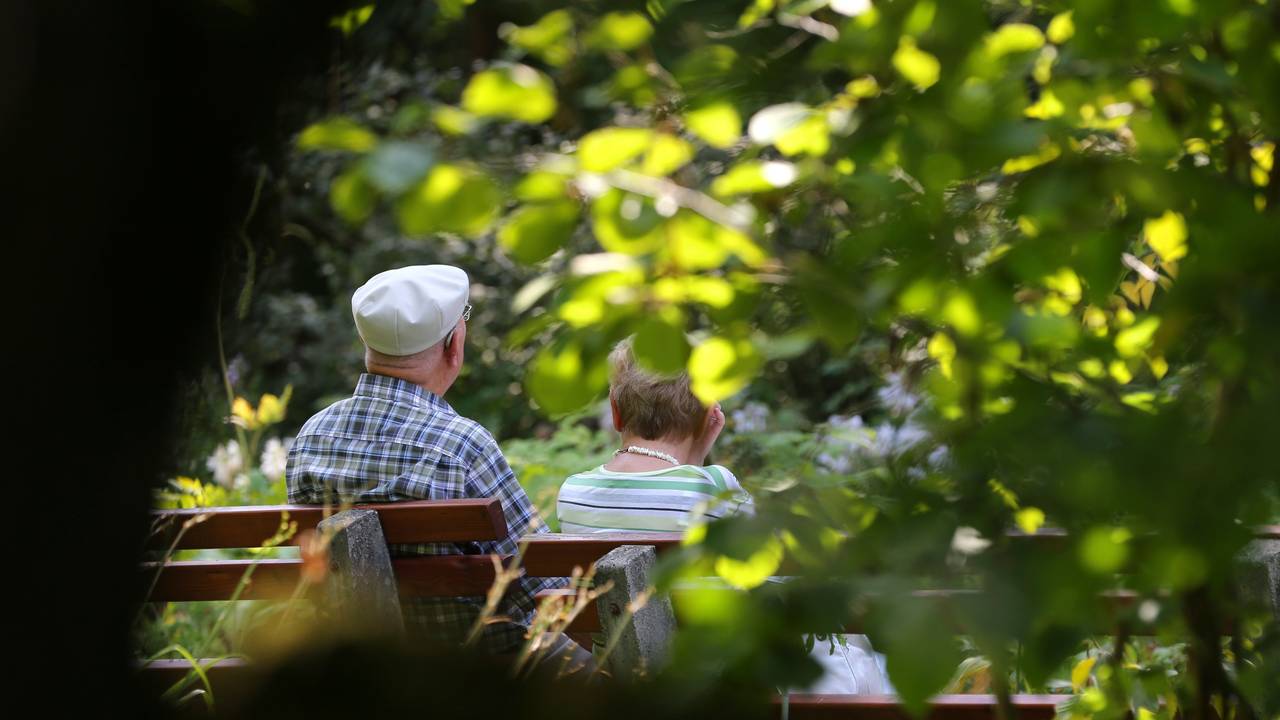 Ein älteres Paar sitzt im Kurpark auf einer Bank im Sonnenschein.