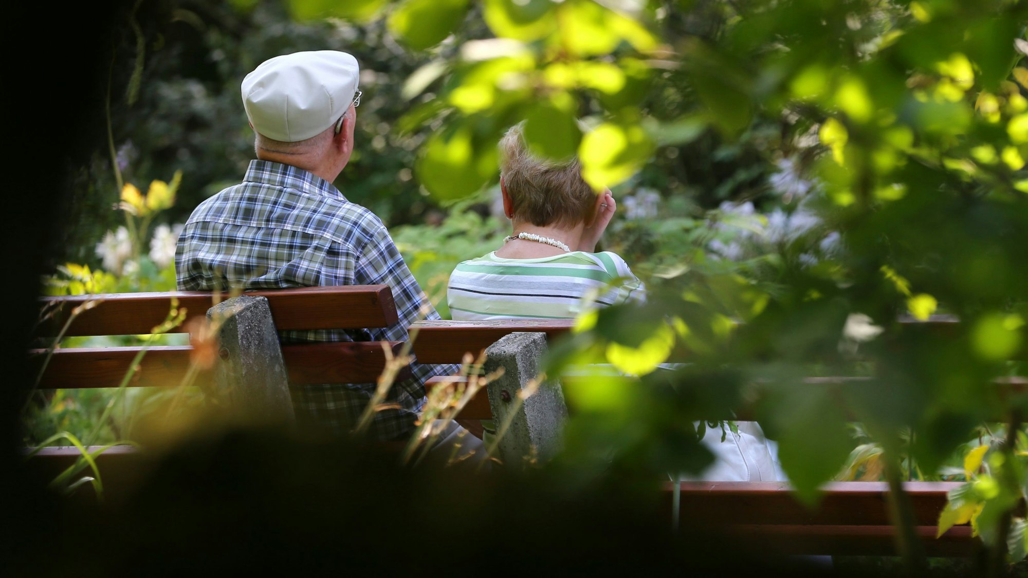 Ein älteres Paar sitzt im Kurpark auf einer Bank im Sonnenschein.