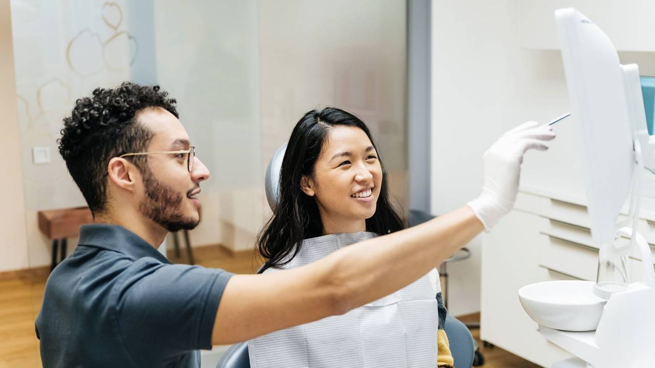 A young patient looking at a monitor and talking to her dentist about her dental health during a check up at his clinic.