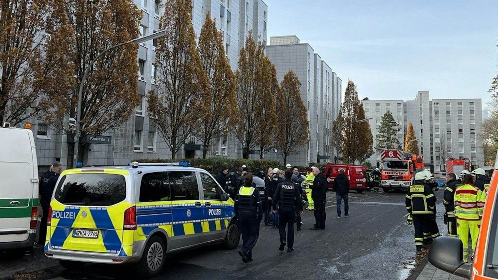 Auf der Straße vor mehreren Wohnkomplexen stehen zahlreiche Einsatzkräfte und -fahrzeuge von Polizei, Feuerwehr und Rettungsdienst.