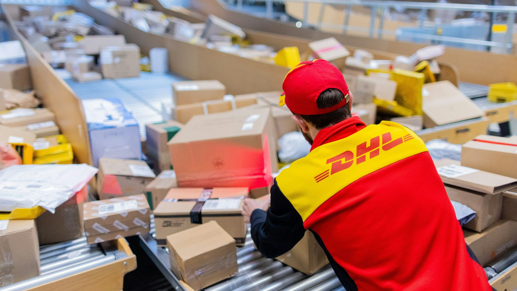 Ein Paketzusteller sortiert und räumt in einer Zustellbasis von Deutsche Post DHL Pakete in ein Zustellfahrzeug.