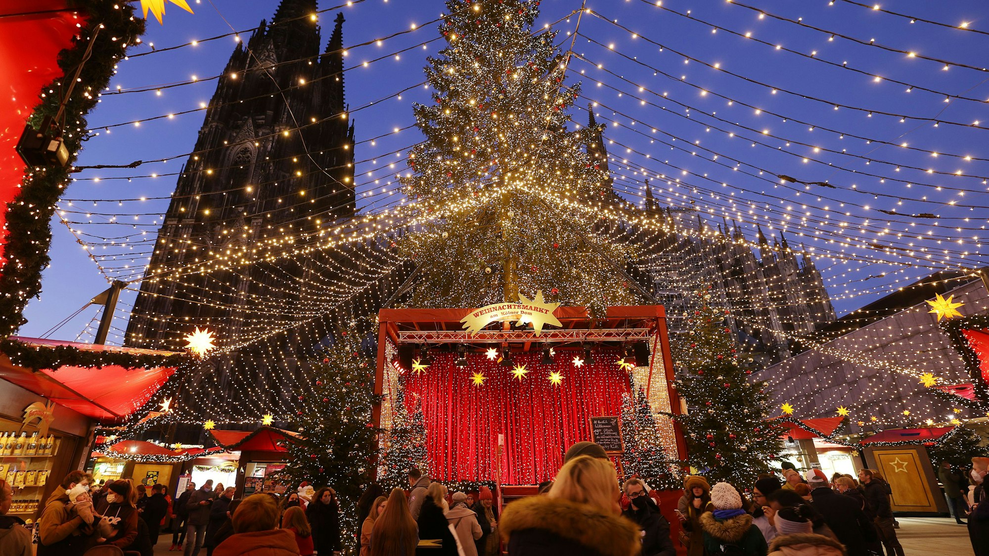 Besucher gehen über den Weihnachtsmarkt auf dem Roncalliplatz am Dom.