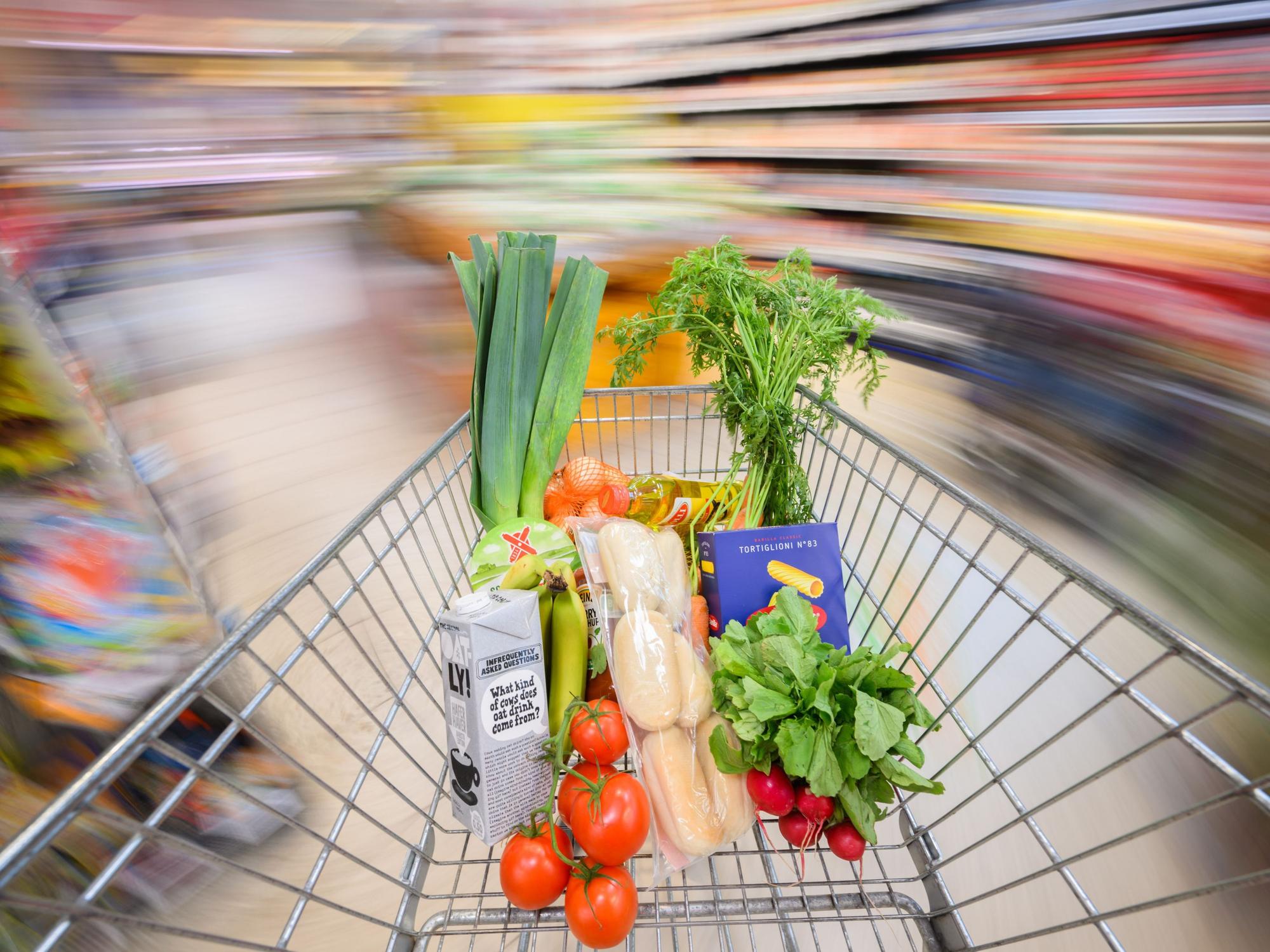 Ein mit Lebensmittel gefüllter Einkaufswagen wird durch einen Supermarkt geschoben.