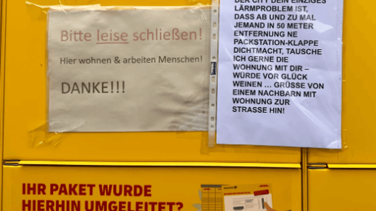 Das Bild zeigt eine DHL-Packstation, an der zwei Zettel hängen, auf denen sich Anwohnenden über den Lärm beschweren