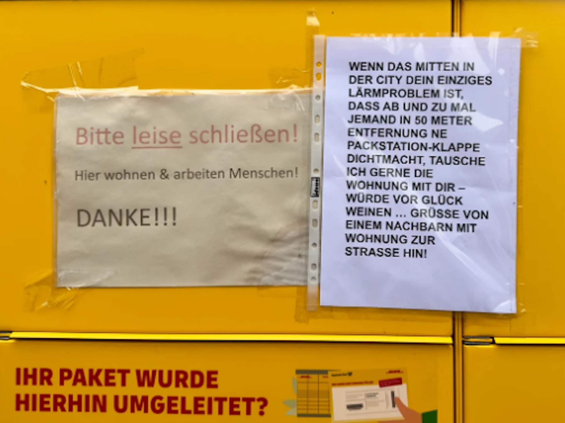 Das Bild zeigt eine DHL-Packstation, an der zwei Zettel hängen, auf denen sich Anwohnenden über den Lärm beschweren