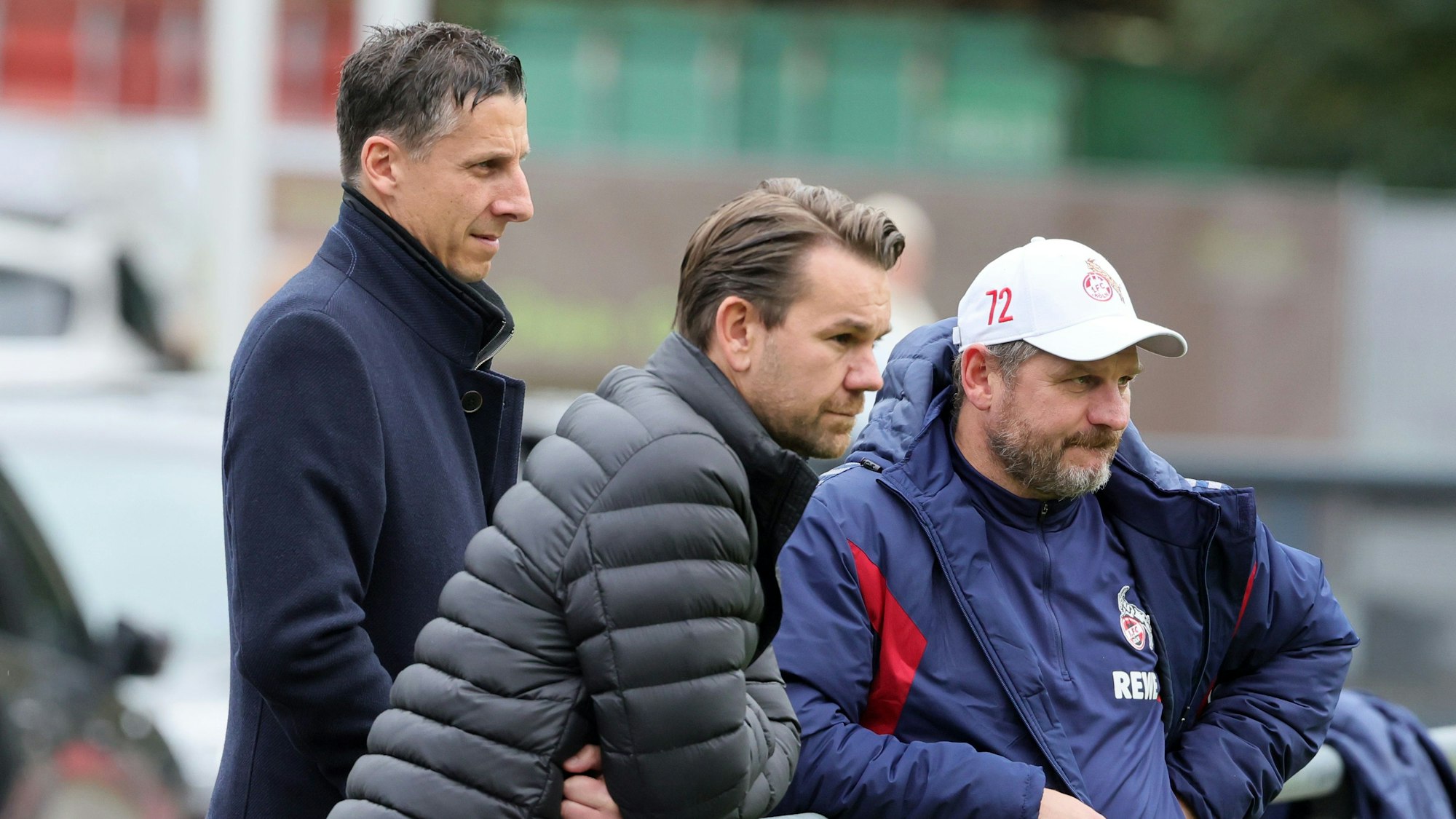 Christian Keller, Thomas Kessler und Steffen Baumgart stehen bei einer Trainingseinheit des 1. FC Köln am Geißbockheim an der Bande.