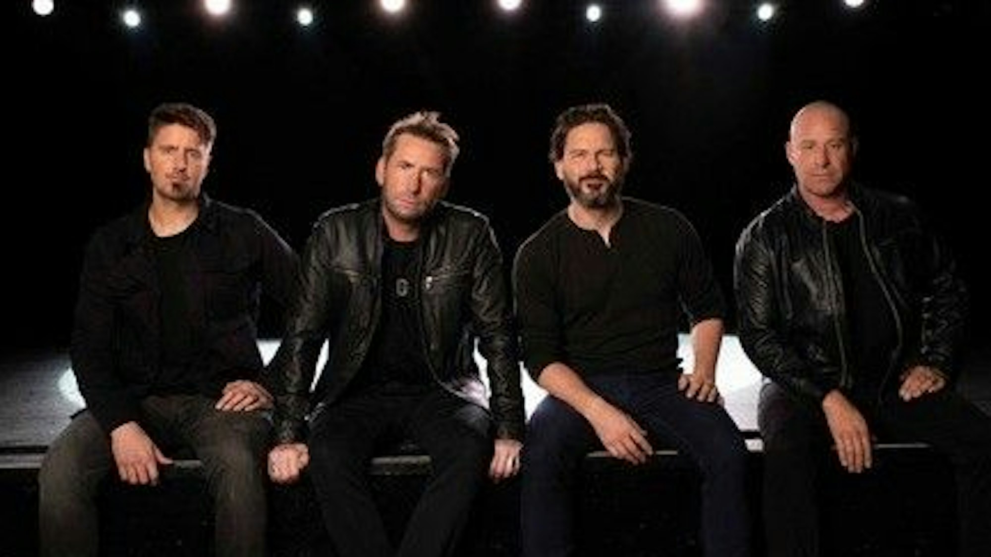 Die Band Nickelback sitzt in schwarzen Klamotten vor der Kamera.